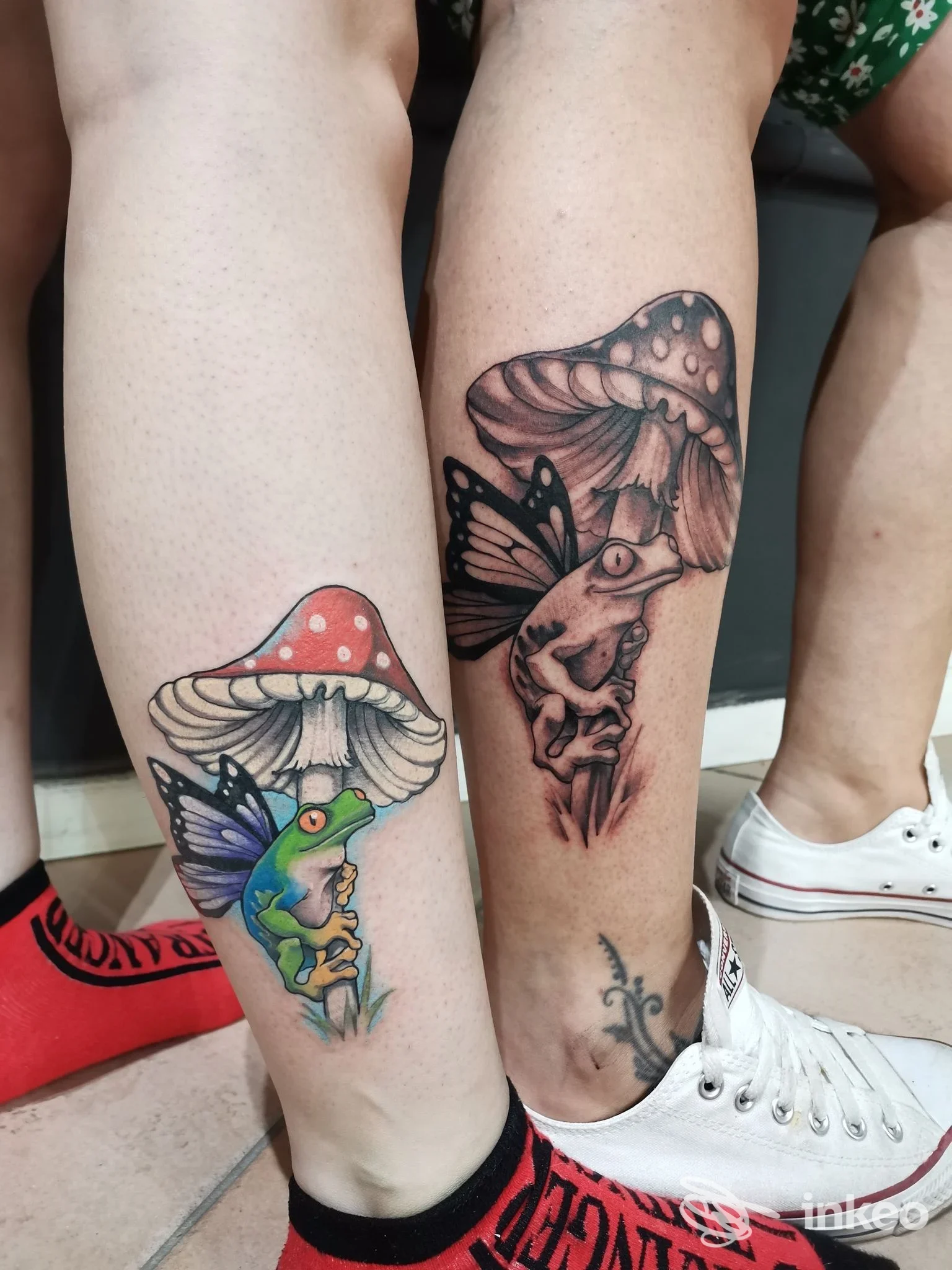 Due tatuaggi su gamba: una rana colorata su fungo sulla gamba sinistra e un uccello stilizzato su fungo con altri elementi decorativi sull’altra gamba, senza volto visibile.