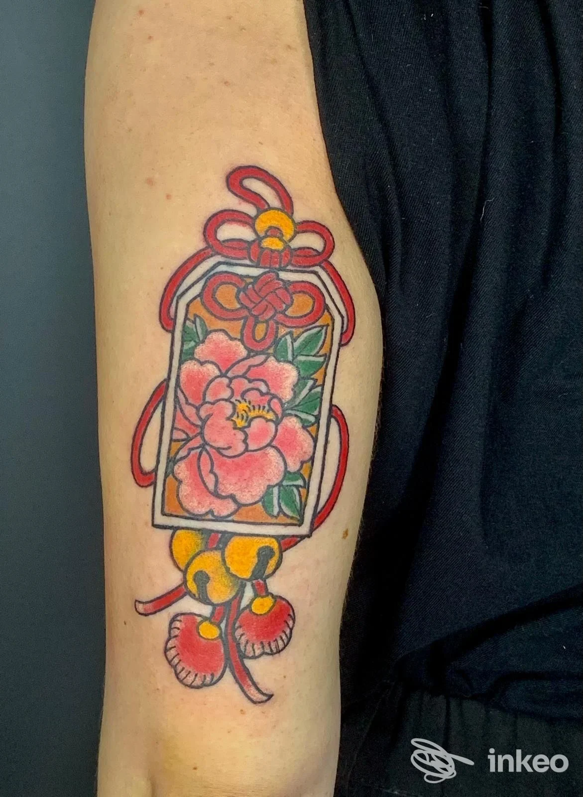Tatuaggio a colori su braccio raffigurante un barattolo decorato con fiori rosa, cordoncino rosso e ciondoli pendenti; realizzazione chiaramente visibile sulla pelle.