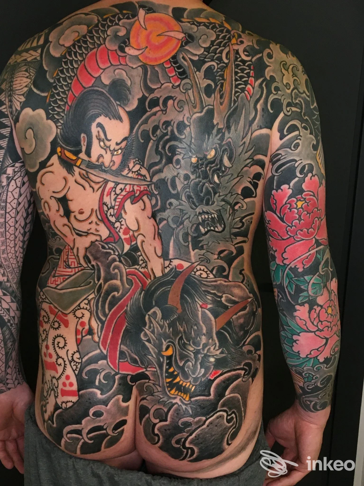 Tattoo esteso sulla schiena raffigurante un guerriero in combattimento con un drago, stile tradizionale giapponese, colori scuri con dettagli rossi e verdi, coprente tutta la schiena.