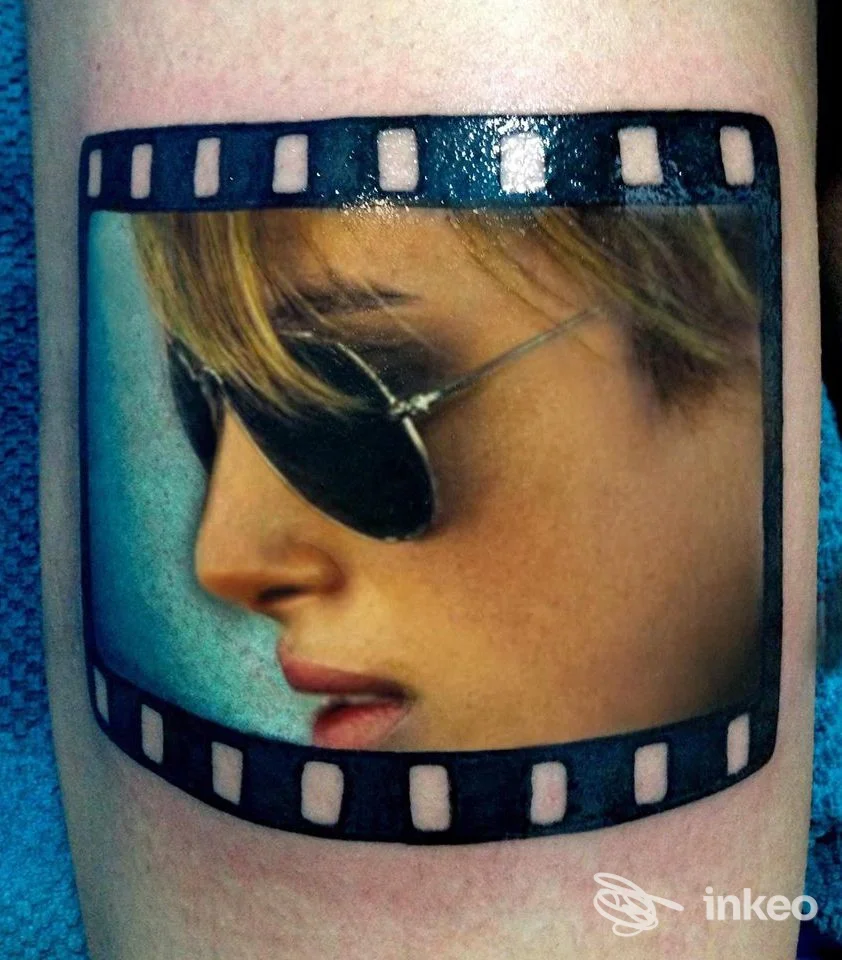 Tattoo su pelle raffigurante un ritratto di una persona con occhiali da sole, incorniciato come una pellicola fotografica.