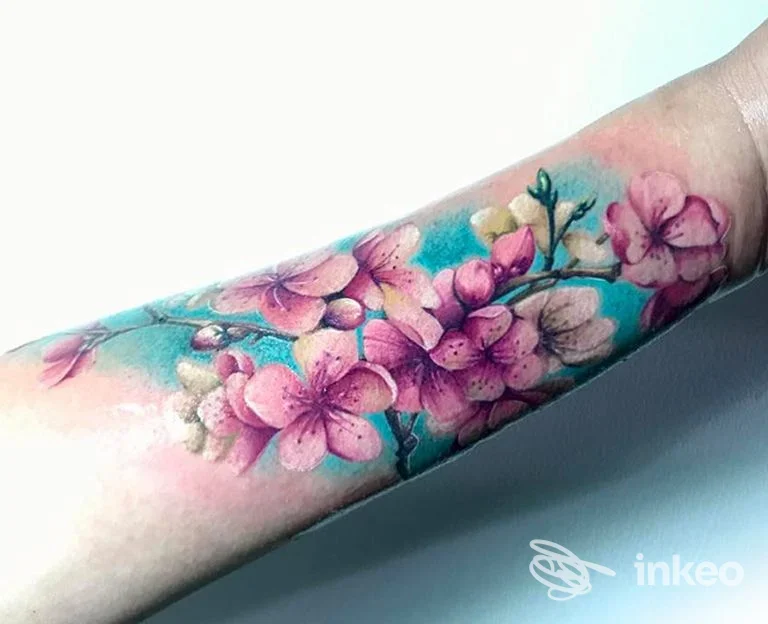 Tattoo colorato di fiori rosa su avambraccio, sfondo azzurro; tattoo pienamente visibile su pelle, nessun volto prominente presente.