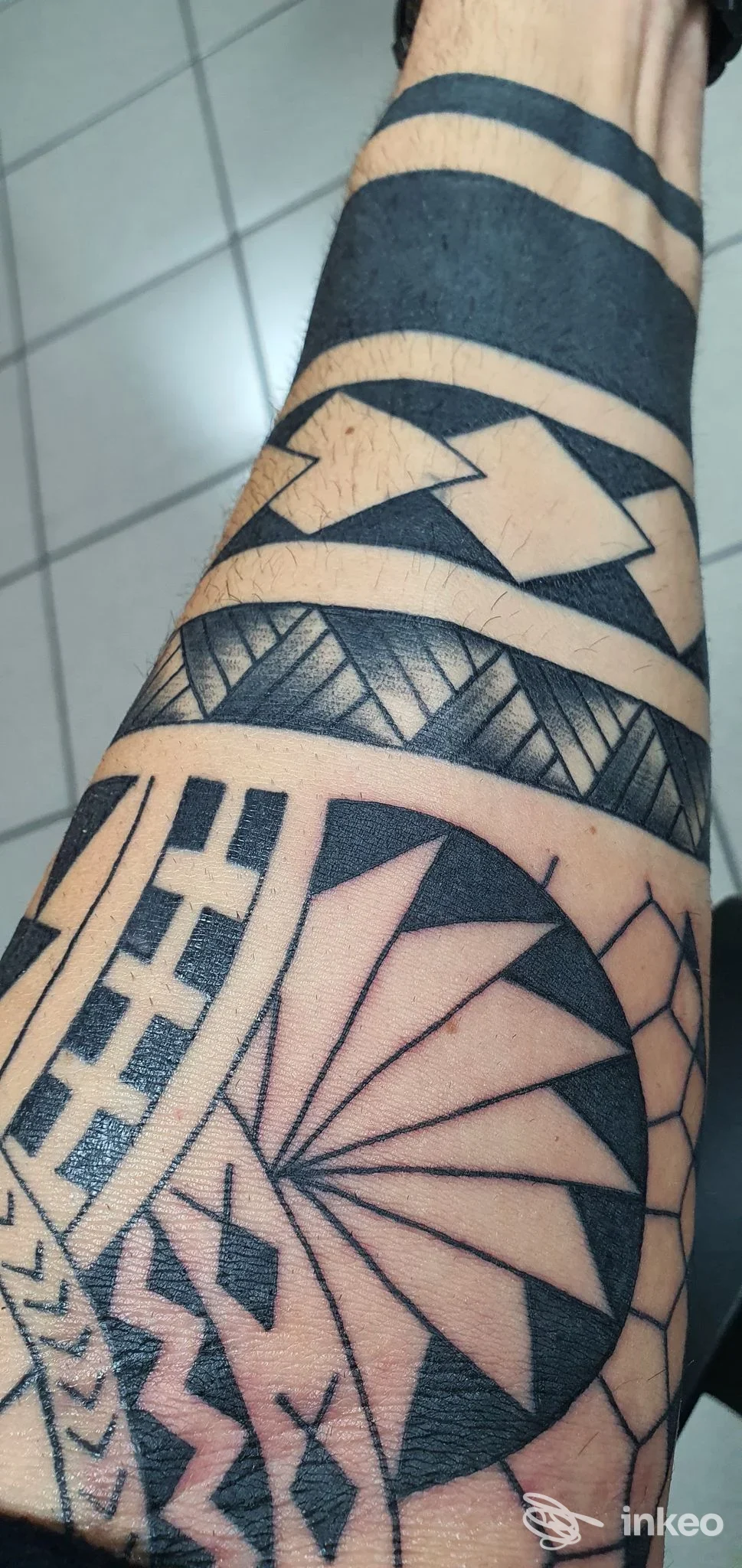 Braccio con tatuaggio geometrico e linee nere su pelle, stile tribale/moderno, visibile una parte significativa del braccio.