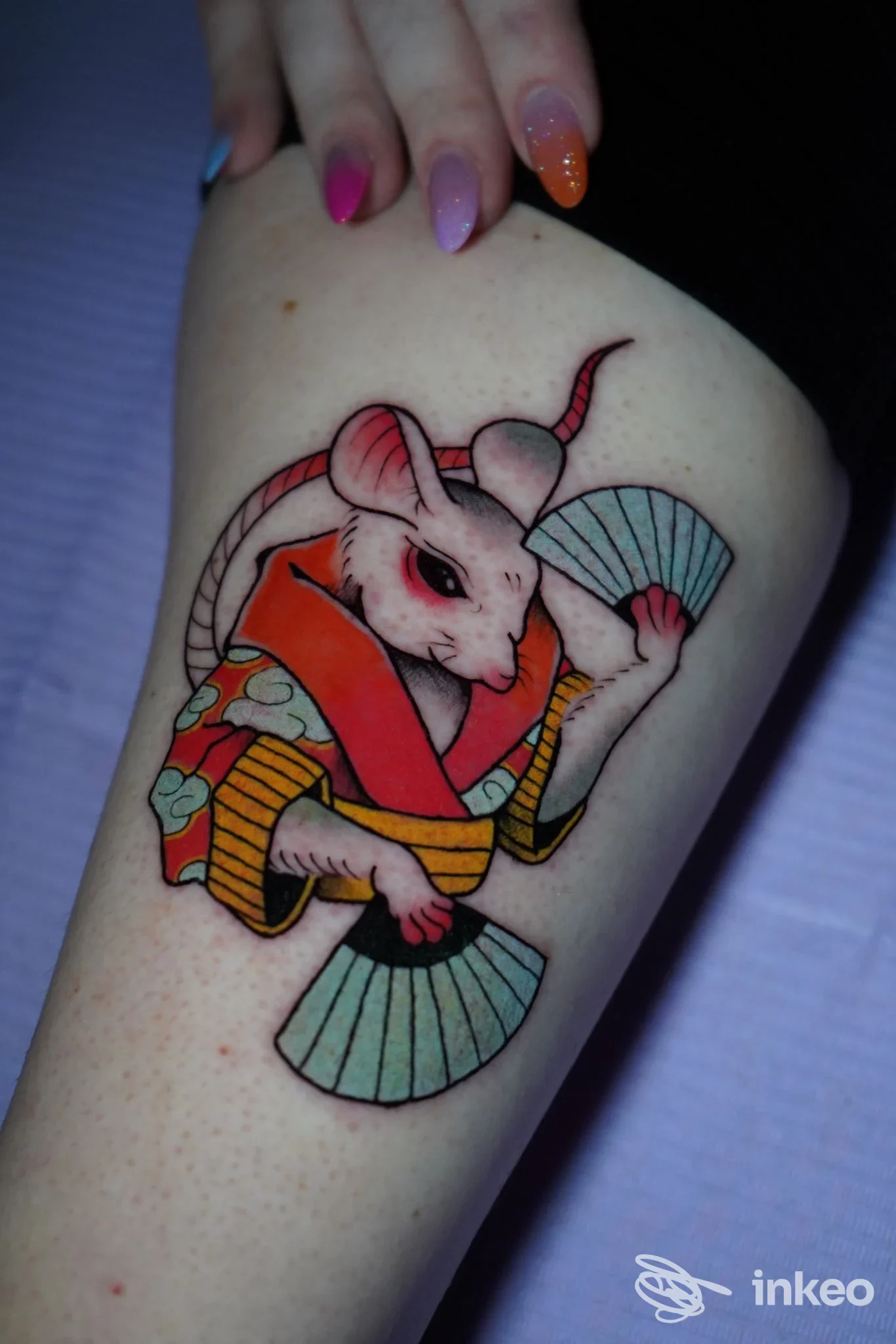 Tatuaggio su avambraccio raffigurante un topo in abito tradizionale con ventagli, colori vivaci e linee nette, realizzato sulla pelle.