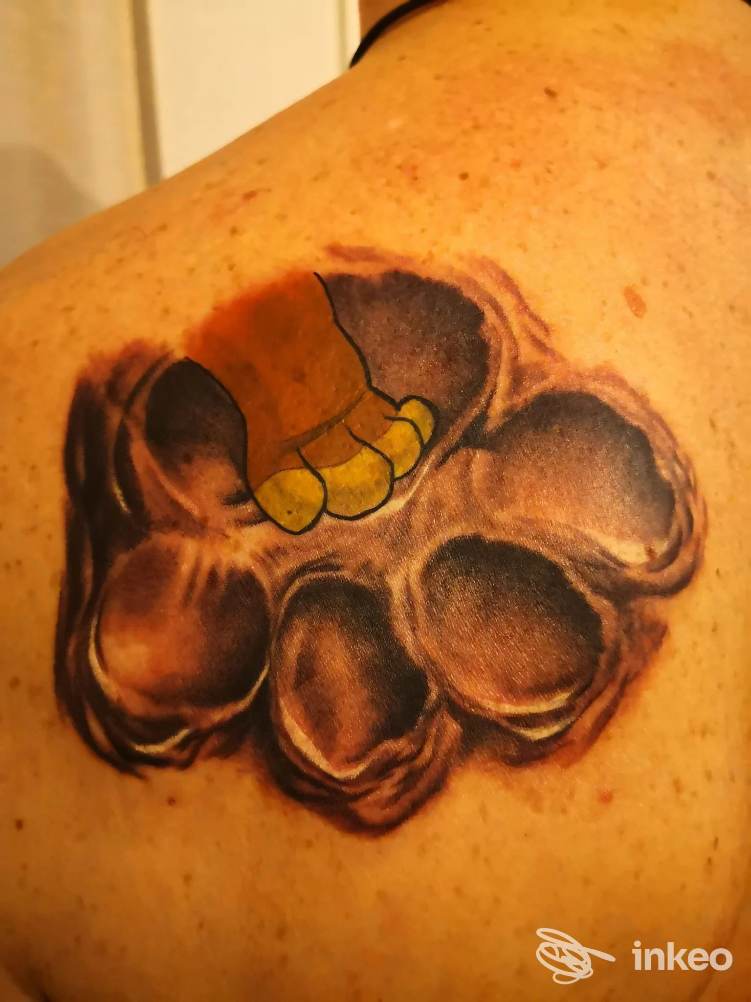 Tattoo oscuro su spalla: una grande forma floreale in colori scuri con riflessi bianchi e dettagli neri, visibile pelle. si nota una piccola parte della nuca vicino, appartenente al corpo; non ci sono elementi di interfaccia sociale.