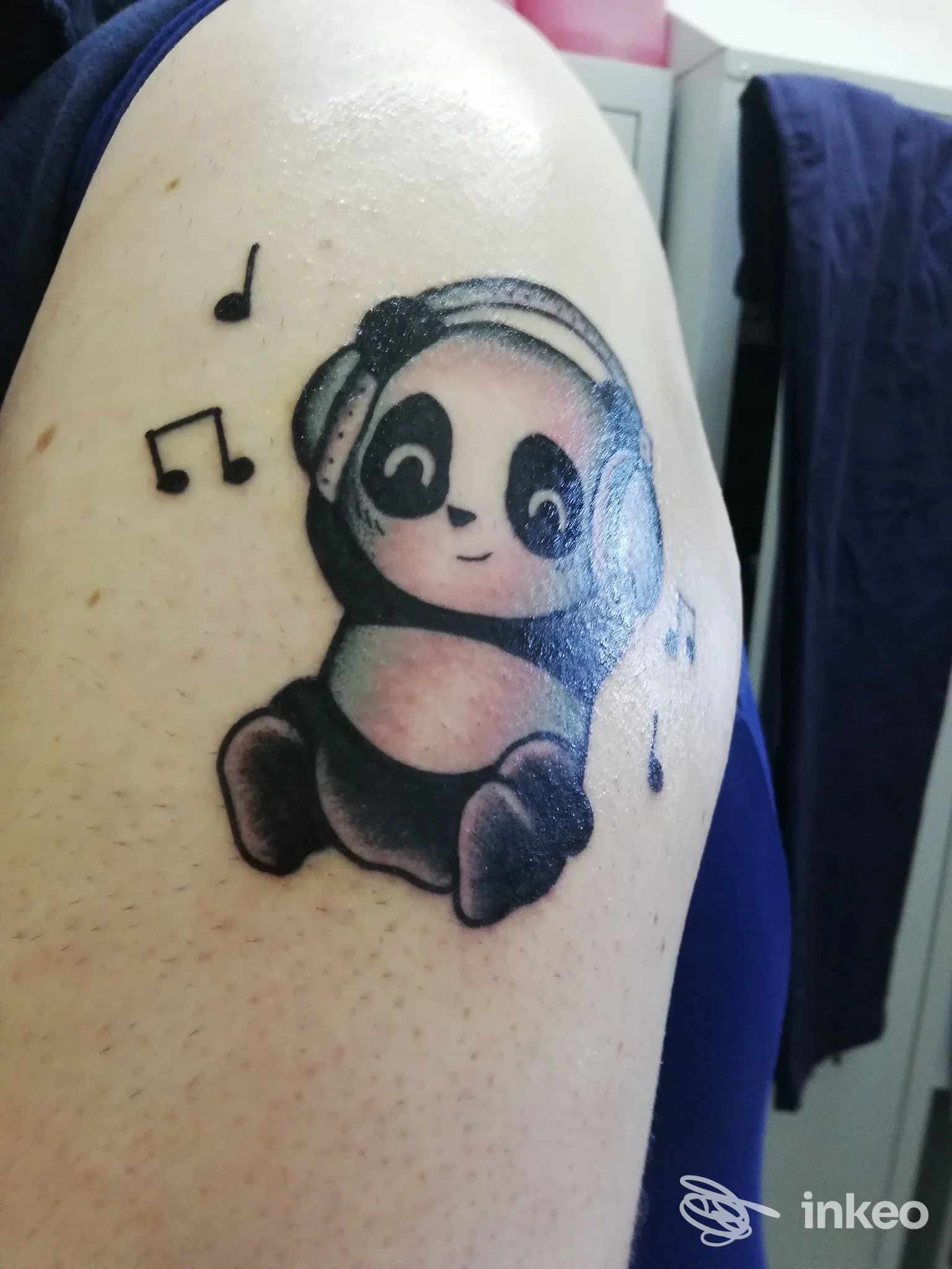 Tatuaggio su braccio superiore raffigurante un panda con cuffie e note musicali, realizzato direttamente sulla pelle.
