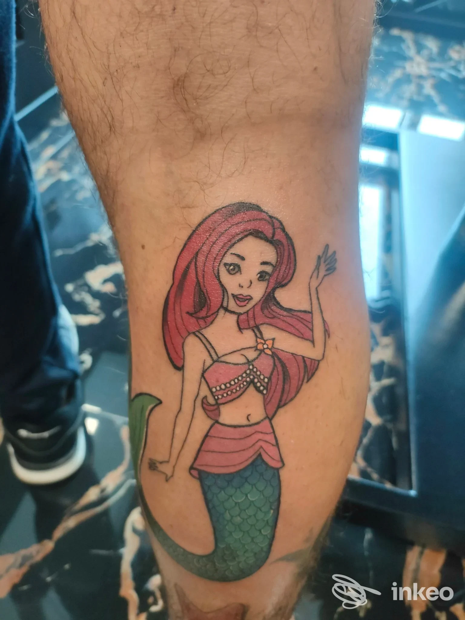 Tattoo raffigurante una sirena con capelli rosa e coda verde, visibile su una gamba, realizzato sulla pelle umana; nessun overlay visivo o testo presente.
