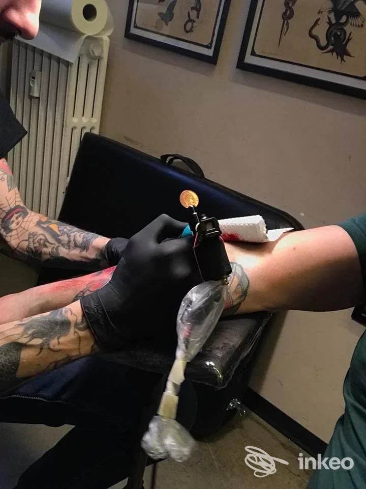 Sulla pelle di un braccio si sta realizzando un tatuaggio; l’artista indossa guanti neri e lavora con una macchina da tatuaggio in uno studio chiamato Best of Times Tattoo.