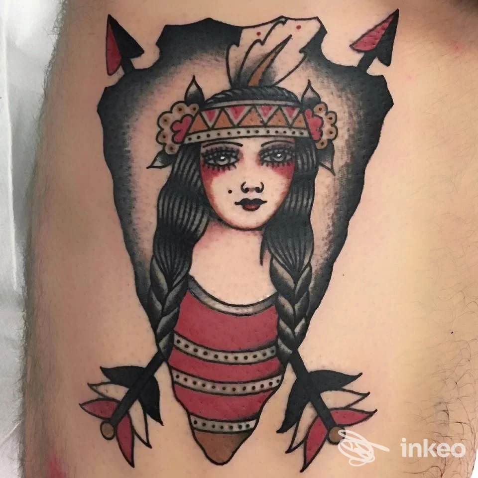 Tattoo raffigurante una ragazza con trecce e copricapo, colori nero, rosso e beige, visibile sulla pelle della parte superiore del braccio/spalla.