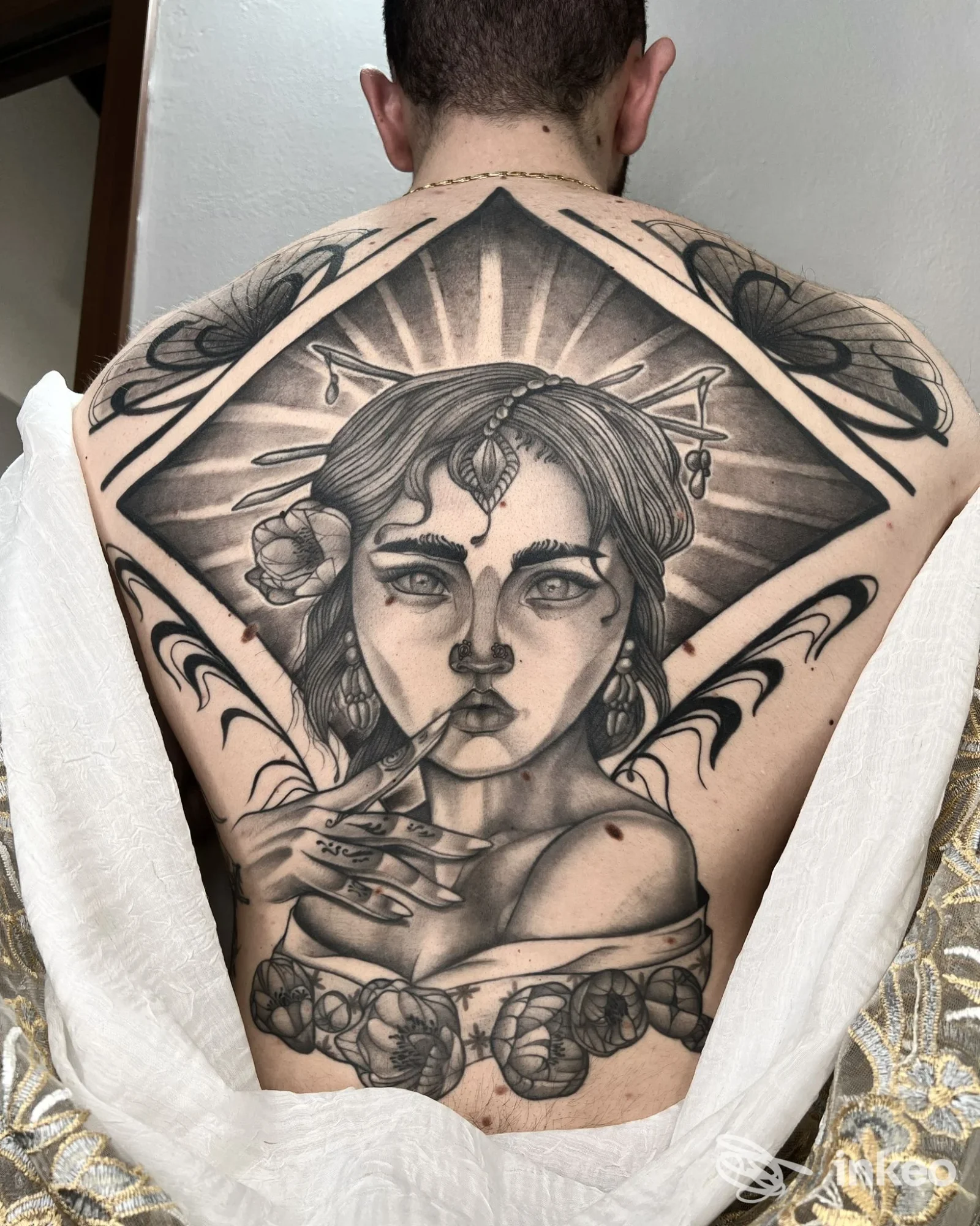 Tattoo realistico in bianco e nero sulla schiena di un uomo: figura femminile incorniciata da un motivo esagonale con sfumature e dettagli, visto di spalle.