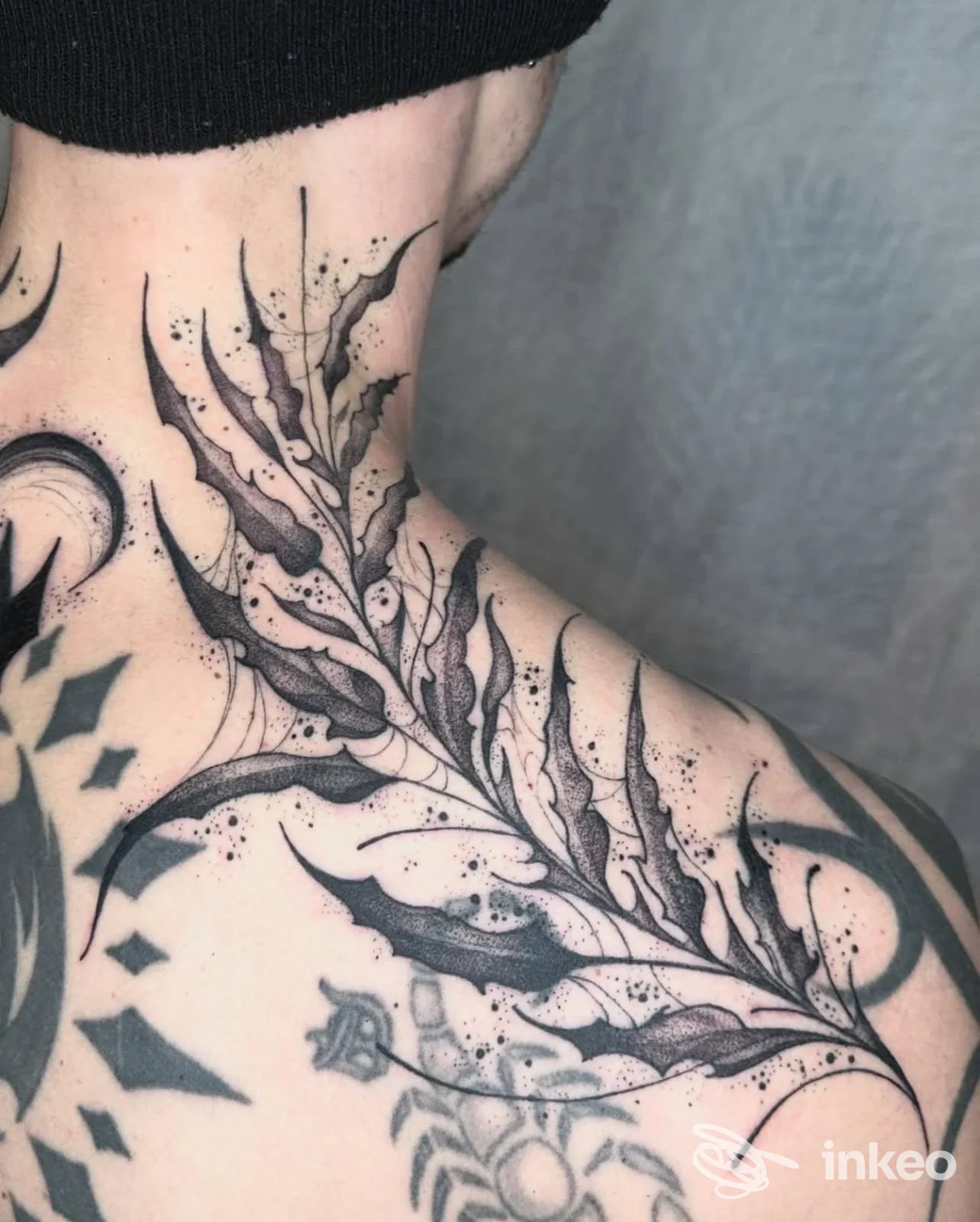 Tattoo originale in nero su collo e spalla sinistra, motivo a foglie con linee fluide e puntini, scatto singolo.