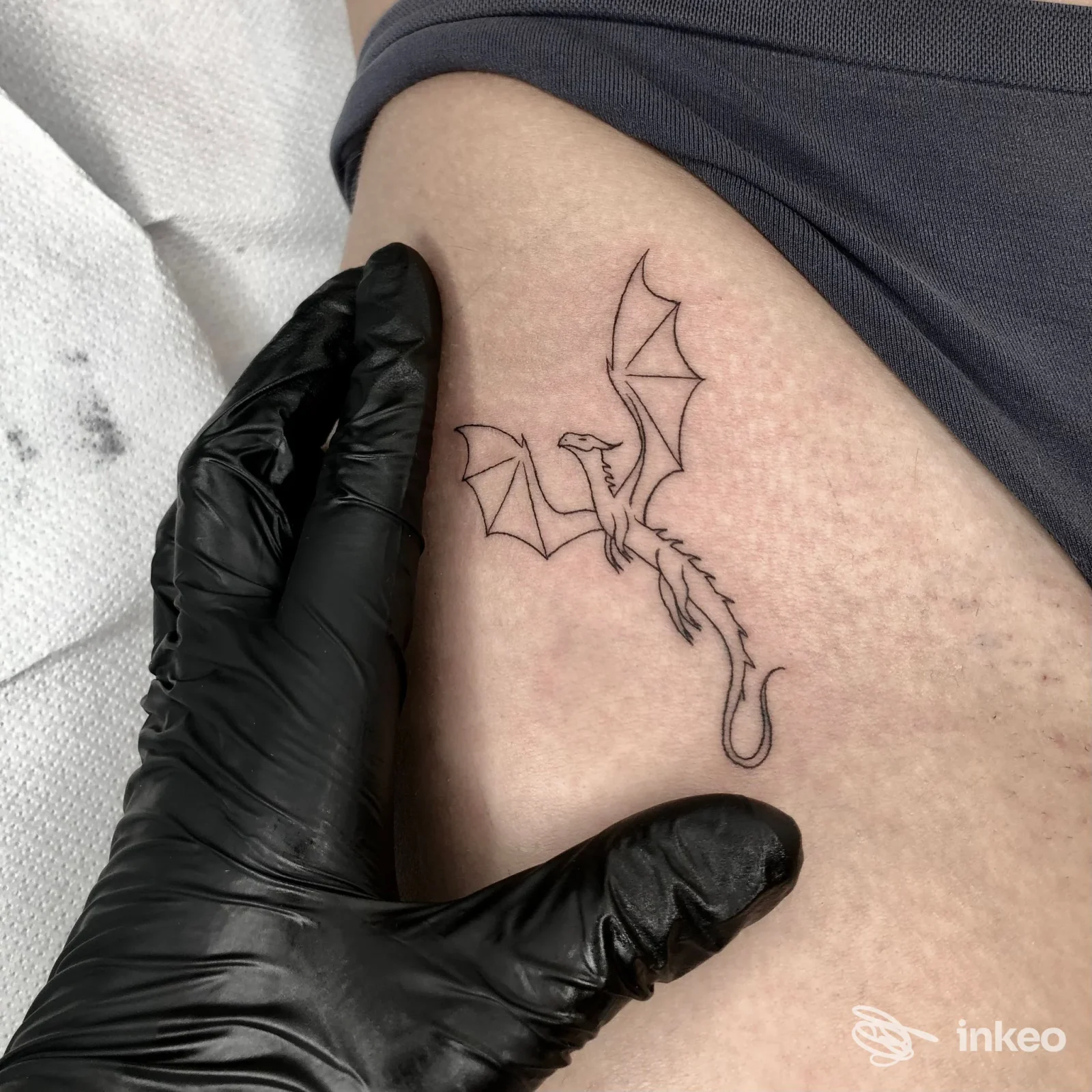 Tattoo di un drago stilizzato su coscia/gamba, realizzato su pelle, con guanto nero a lato, nello studio Elektra Tattoo Lab.