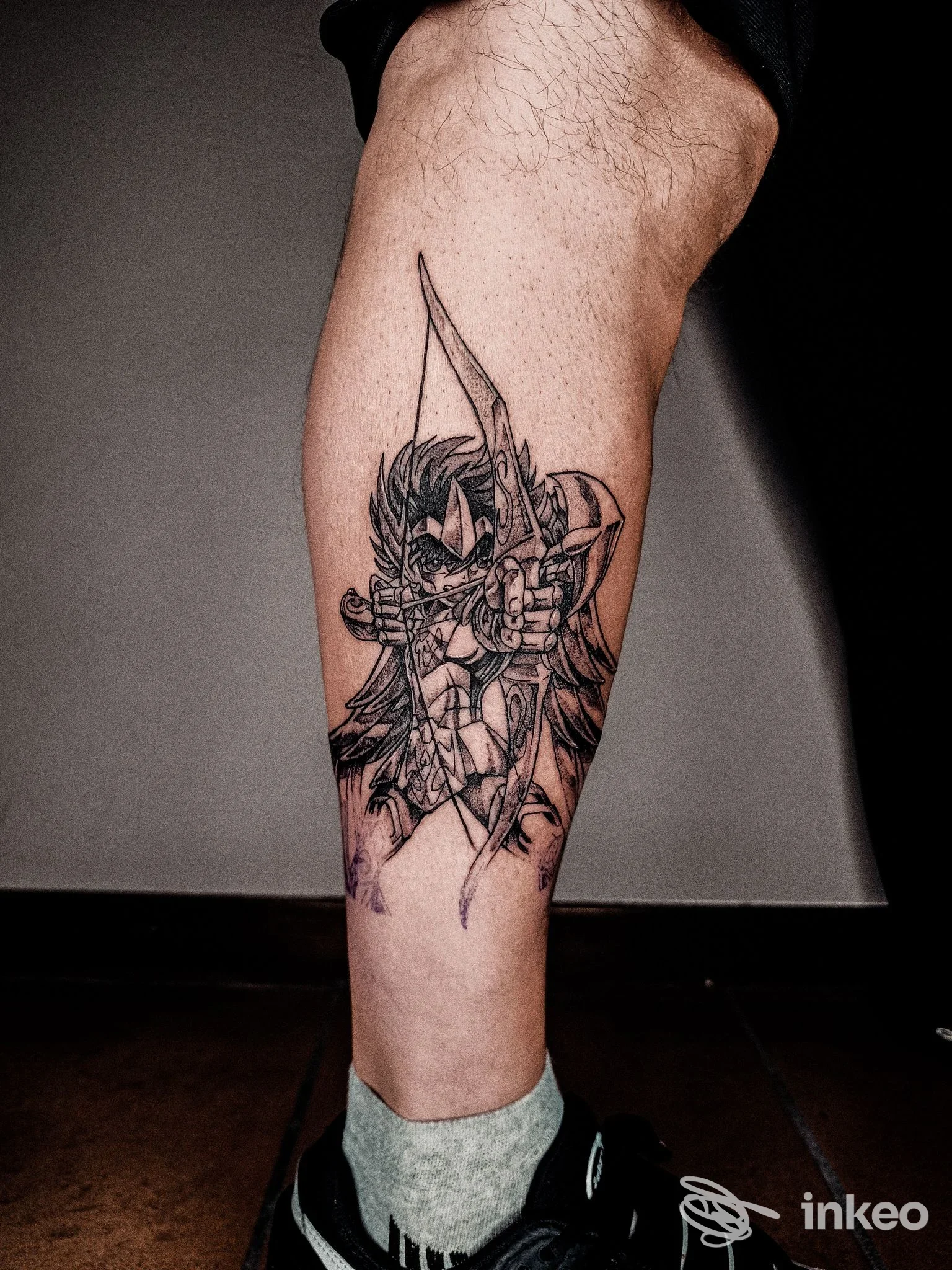 Tattoo sul polpaccio di una persona, tratto da disegno lineare con sfumature grigie, visibile chiaramente su pelle naturale.