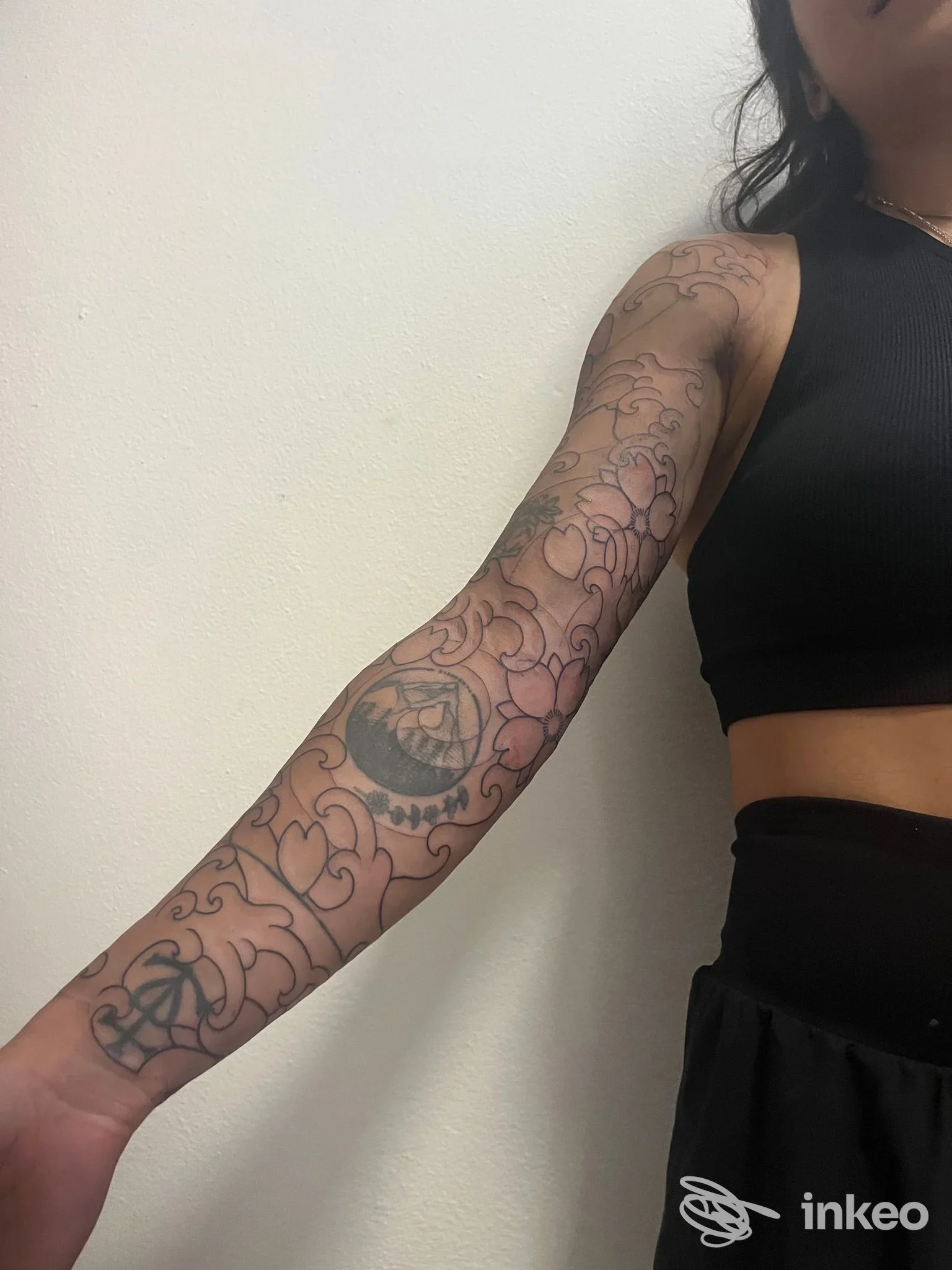 Braccio di una persona con tatuaggio floreale tratteggiato, visibile dall’avambraccio fino al braccio, in un tutore nero, sfondo bianco; studio ĀYU Tattoo Temple a Cremona.