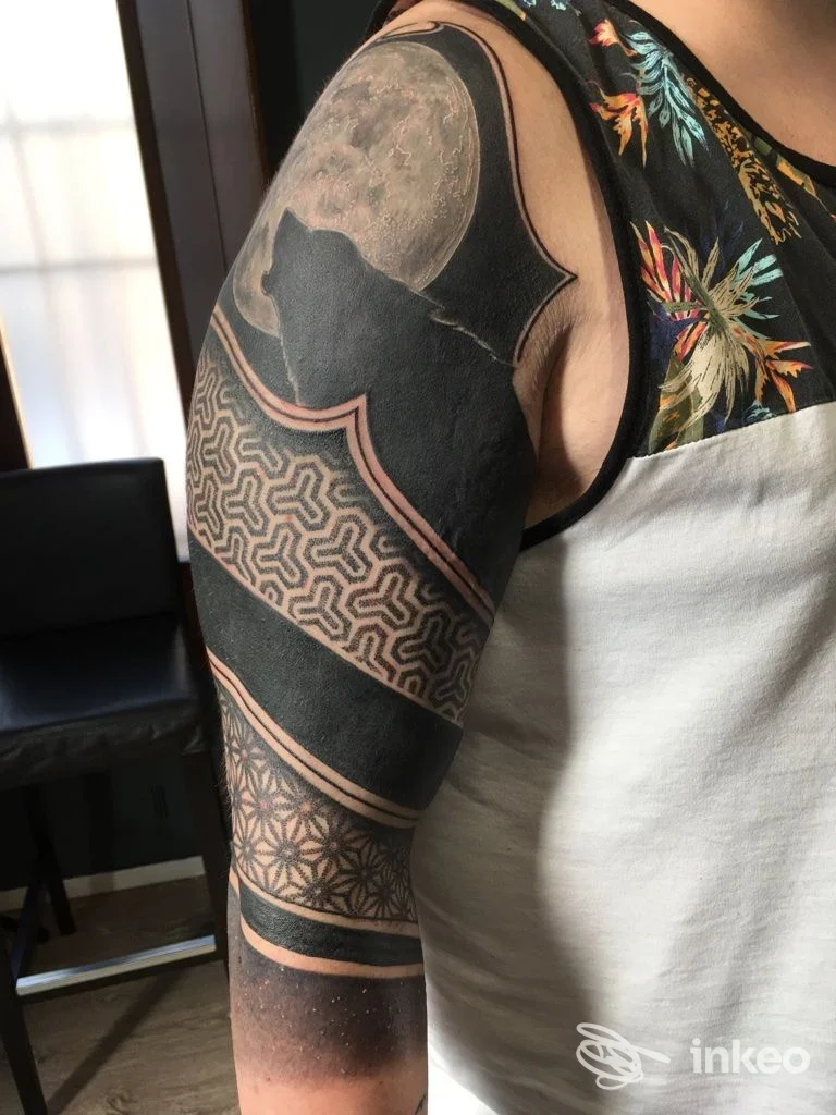Braccio sinistro di una persona con tatuaggio nero e motivi geometrici, contorni rosati, senza volto visibile, scatto ravvicinato dall’angolo laterale.
