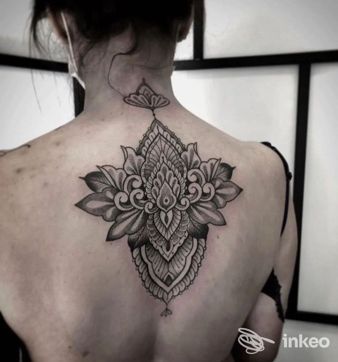 Tattoo grande e dettagliata sulla schiena, motivo mandala con linee nere e sfumature, visibile dall’alto, nessun volto o testo presente, scatto singolo.
