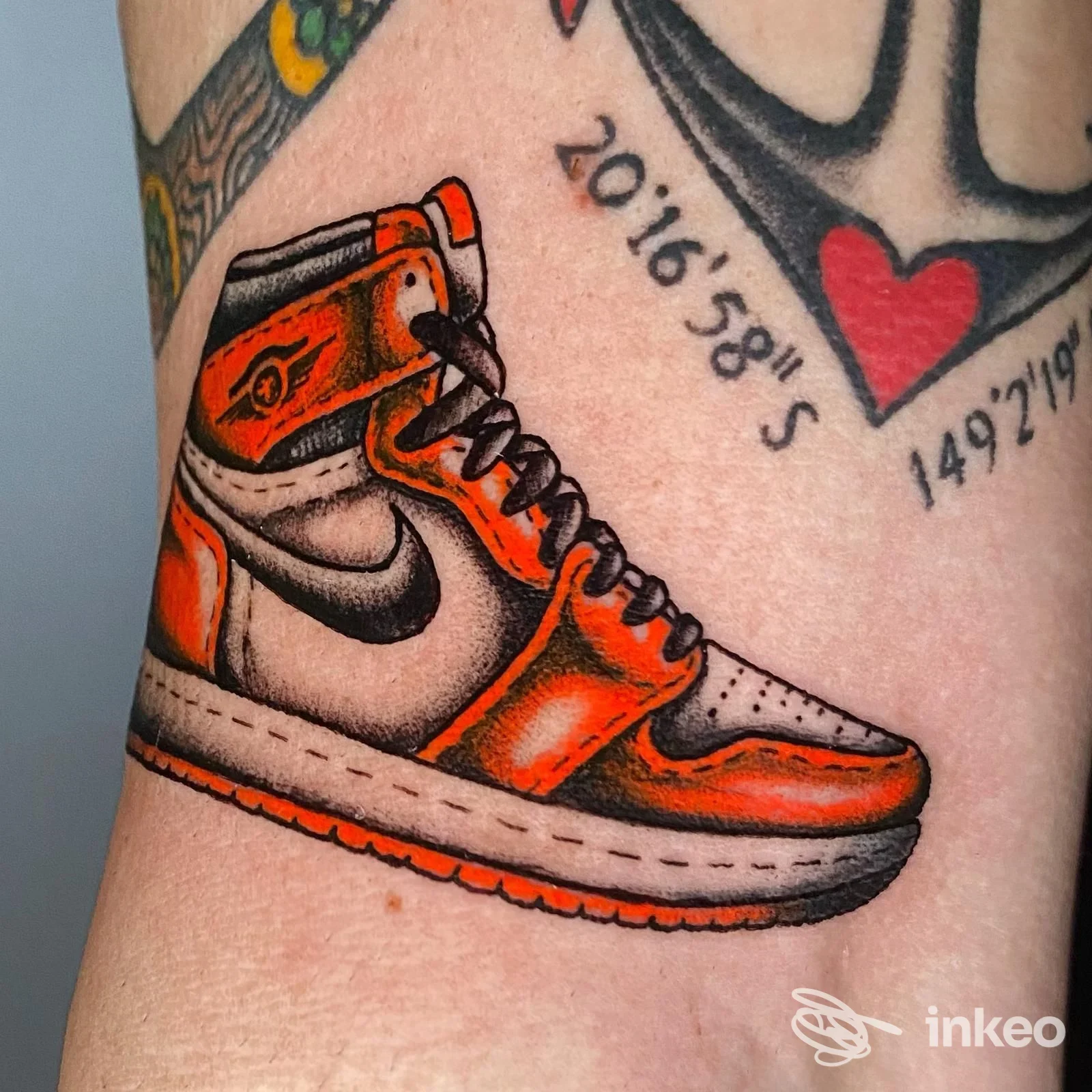 Tatuaggio su pelle raffigurante una sneaker arancione/bianca con dettagli neri, visibile sull’avambraccio; nessun volto o testo promozionale presente.