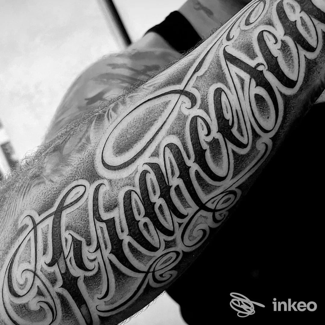 Forearm tattoo in calligraphic style lungo la pelle, senza presenza di volto visibile, scatto verticale in bianco e nero.