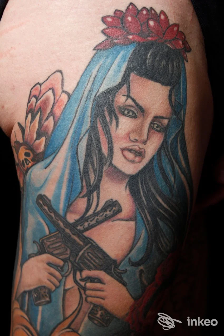 Tatuaggio su pelle di una donna con velo azzurro e coroncina rossa, tenendo due pistole; braccio visibile, senza testo né watermark, realizzato da Inkranium Tattoo.