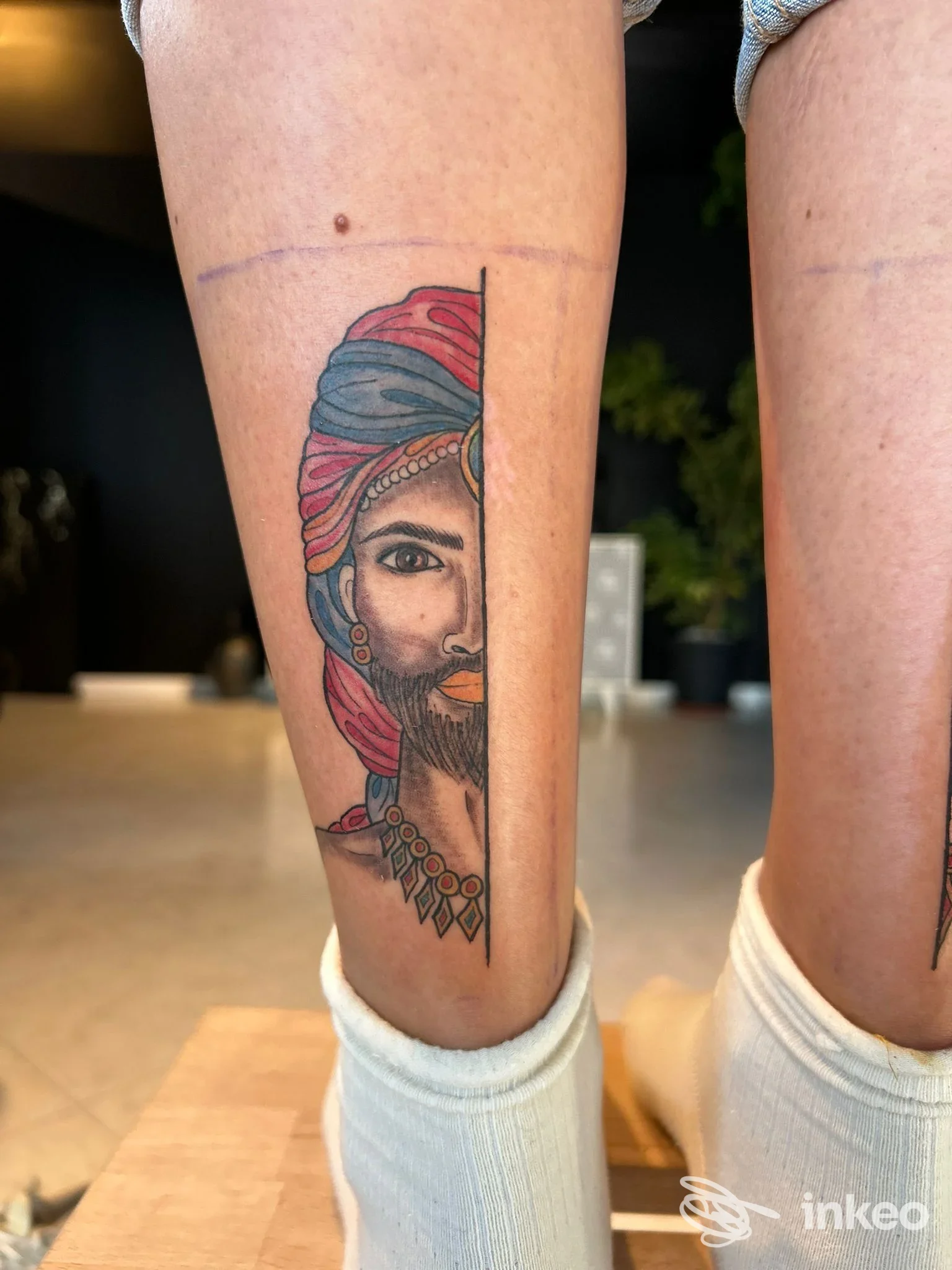 Tatuaggio su polpaccio raffigurante una figura con turbante colorato e barba, realizzato direttamente sulla pelle.