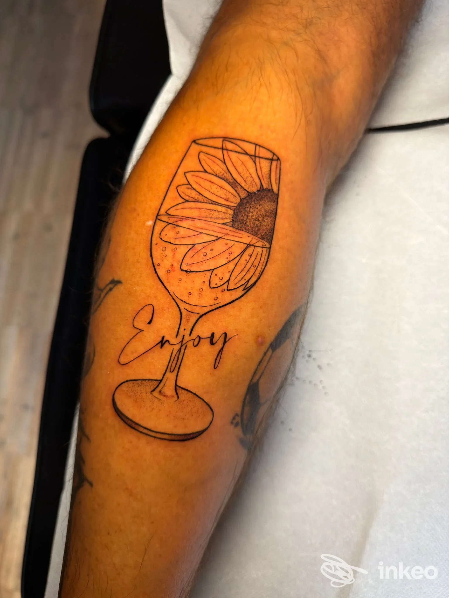 Tattoo su avambraccio raffigurante un bicchiere di vino con un girasole, tratto in linea nera su pelle, stile linework.