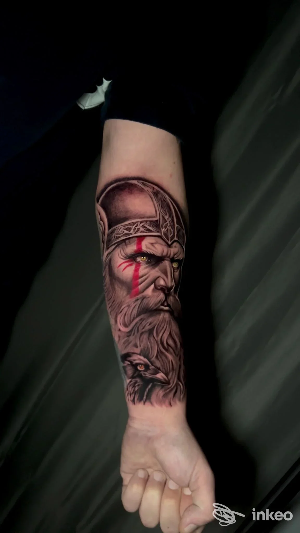 Avambraccio sinistro con tatuaggio realistico di un vecchio guerriero barbuto con elmo, dettagli scuri e sfumature, visibile su pelle reale.