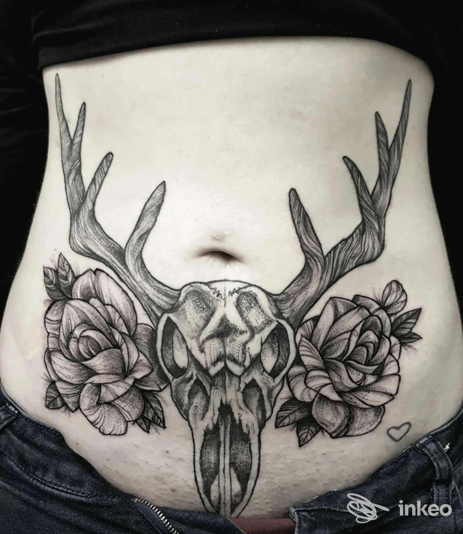 Tattoo a colori nera sull’addome che rappresenta un teschio di cervo con corna, accompagnato da due rose, realizzato sulla pelle.