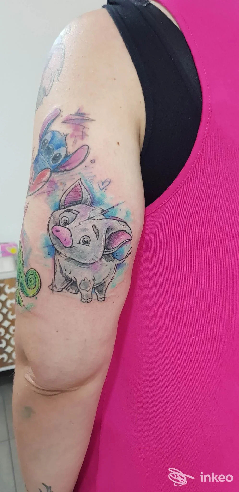 Tattoo colorato su pelle della parte superiore del braccio sinistro: personaggio cartoonesco su sfondo neutro, senza volto visibile.