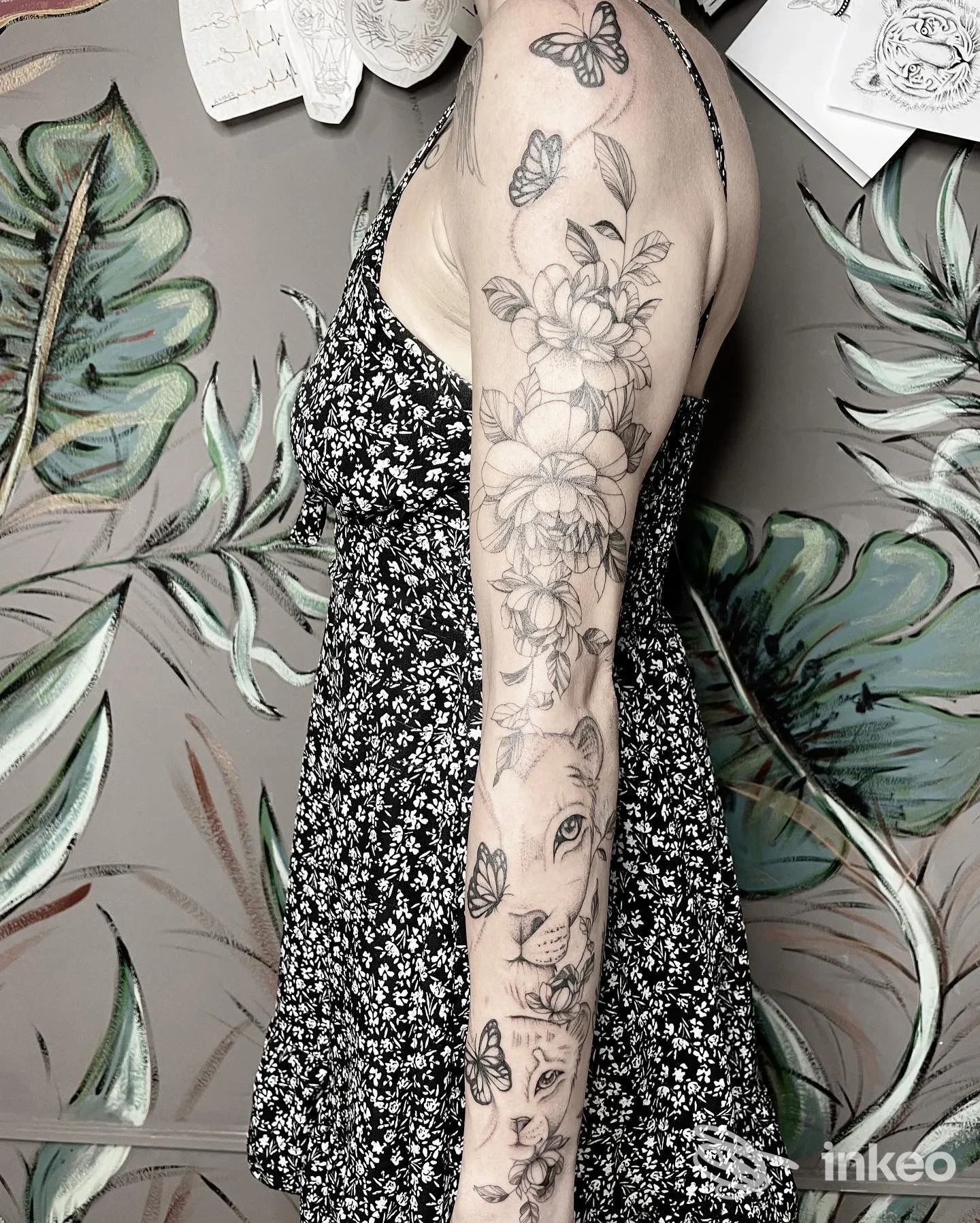 Braccio sinistro di una persona con tatuaggio floreale lungo l’avambraccio, contorni scuri e riempimenti dettagliati, sfondo decorativo.