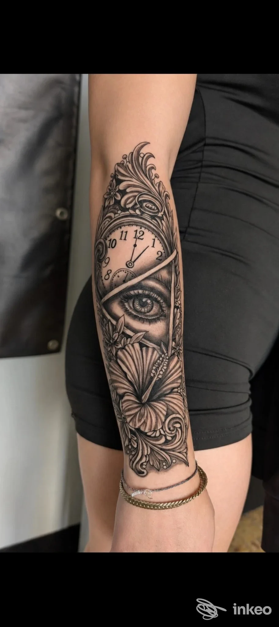 Tattoo in bianco e nero sull'avambraccio: orologio circondato da motivi decorativi con un occhio centrale, realizzato direttamente sulla pelle.