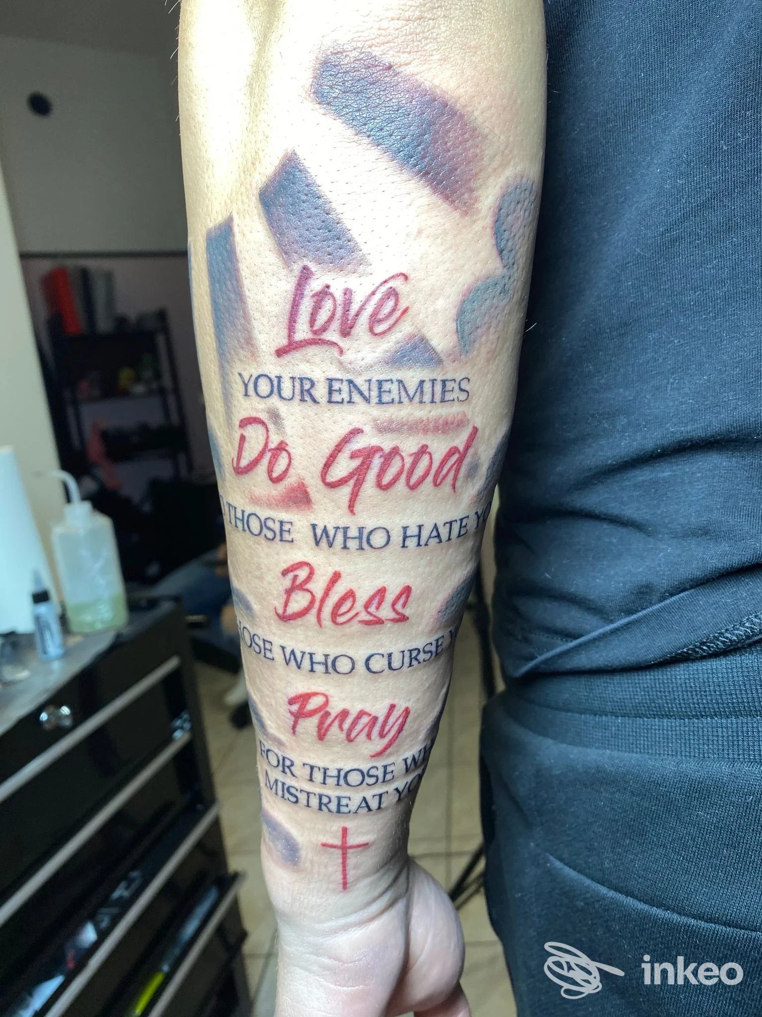 Tattoo sull'avambraccio con testo religioso/etico: Love Your Enemies, Do Good, Those Who Hate, Bless, Pray.
