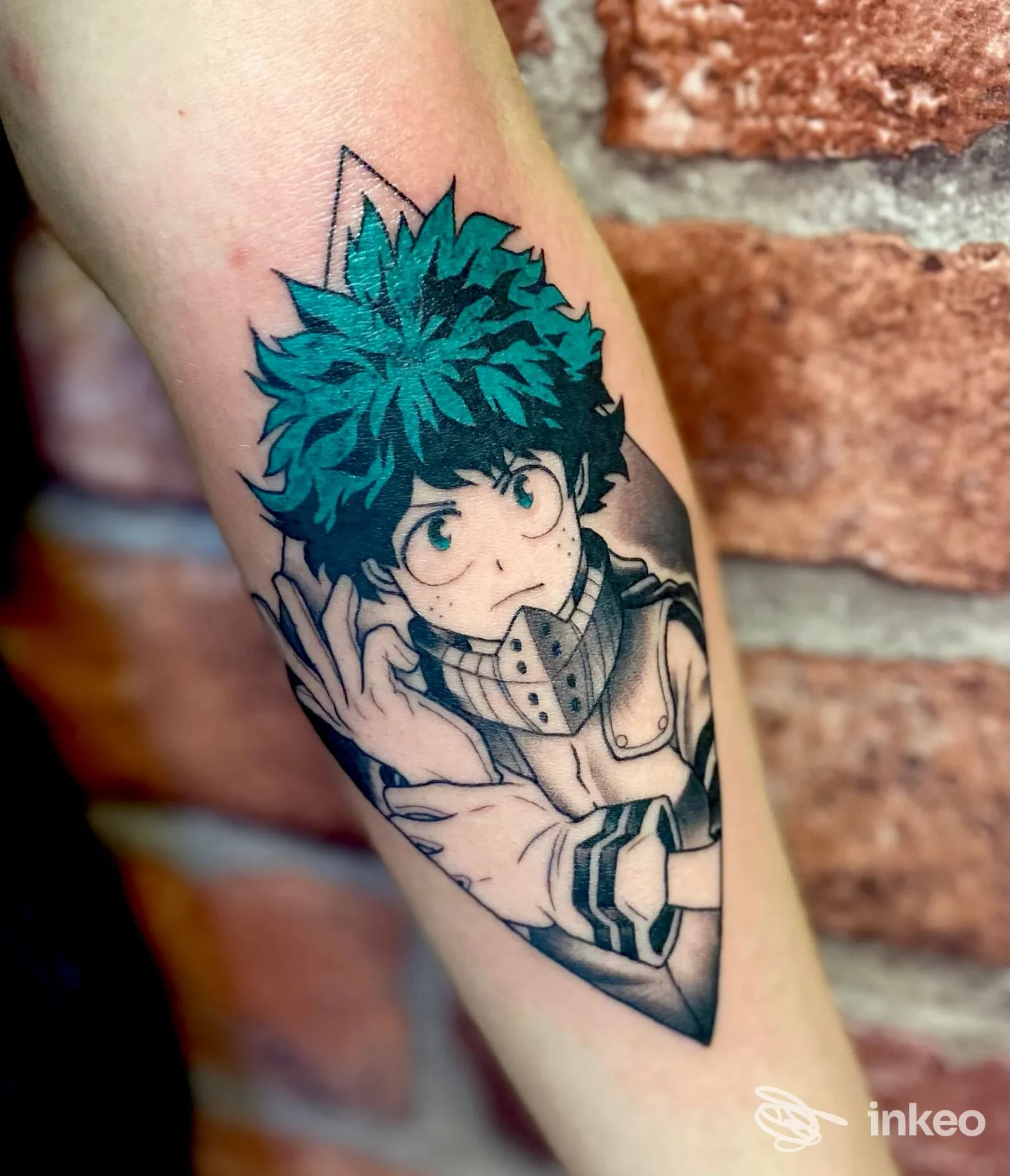 Tattoo su avambraccio raffigurante Deku, personaggio di anime, con linee nette e colori azzurro intenso, incorniciato da una cornice grafica.
