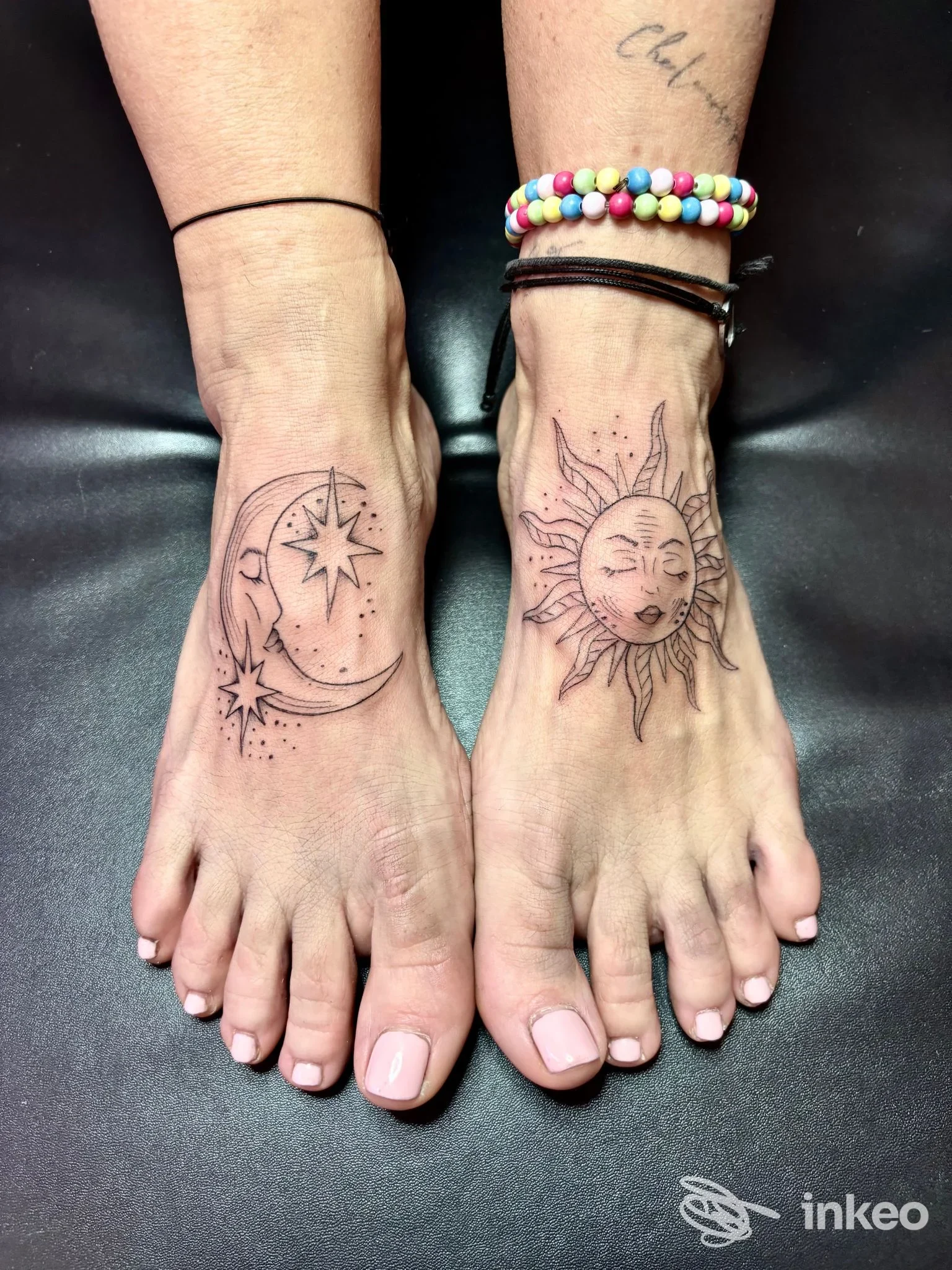 Due piedi con tatuaggi: sul sinistro luna e stelle, sul destro sole con volto, visibili su pelle reale.