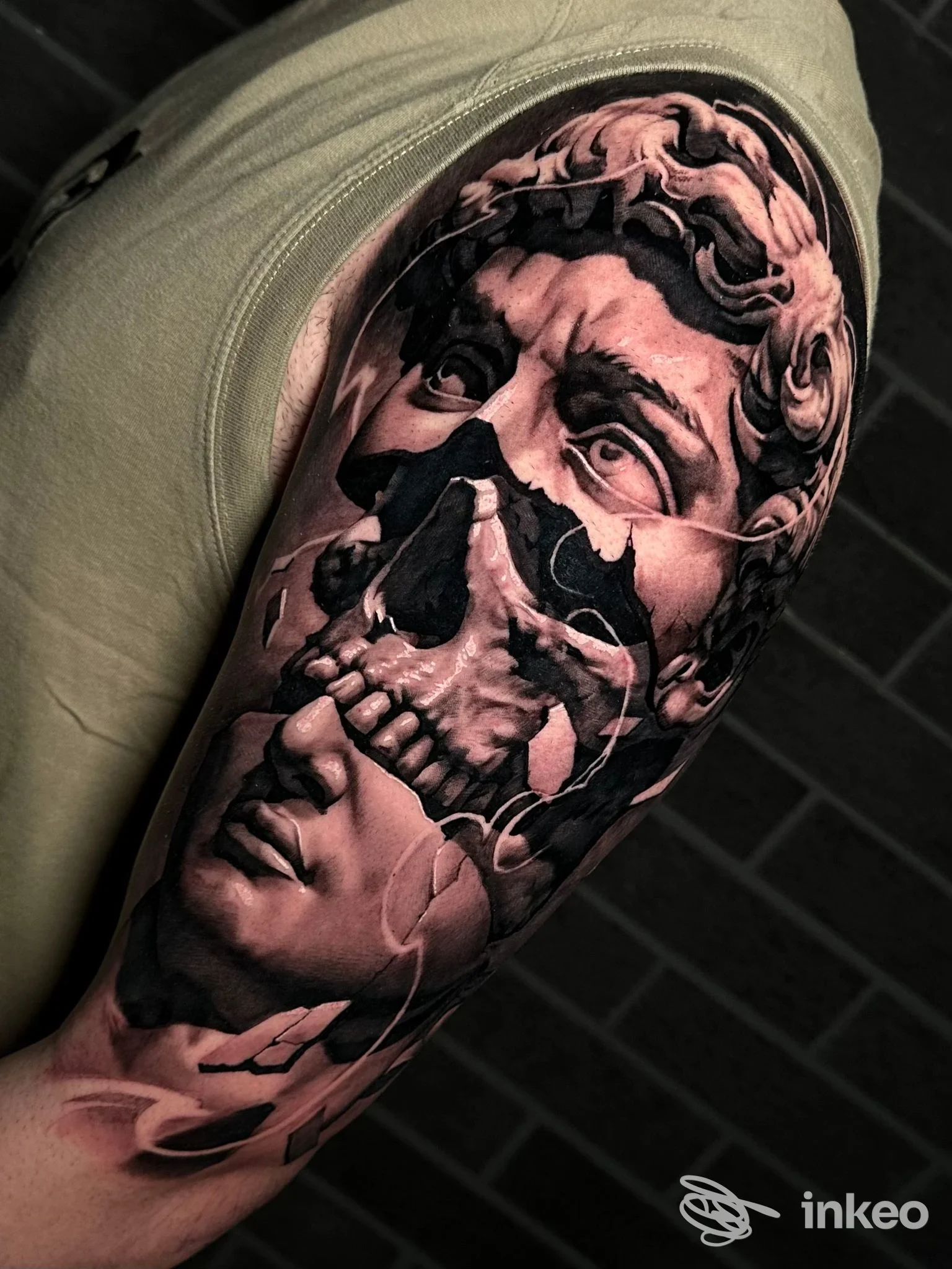 Tattoo realistico su braccio raffigurante un teschio sovrapposto a una scultura; tonalità in bianco e nero, dettaglio elevato, senza testo o elementi promozionali.