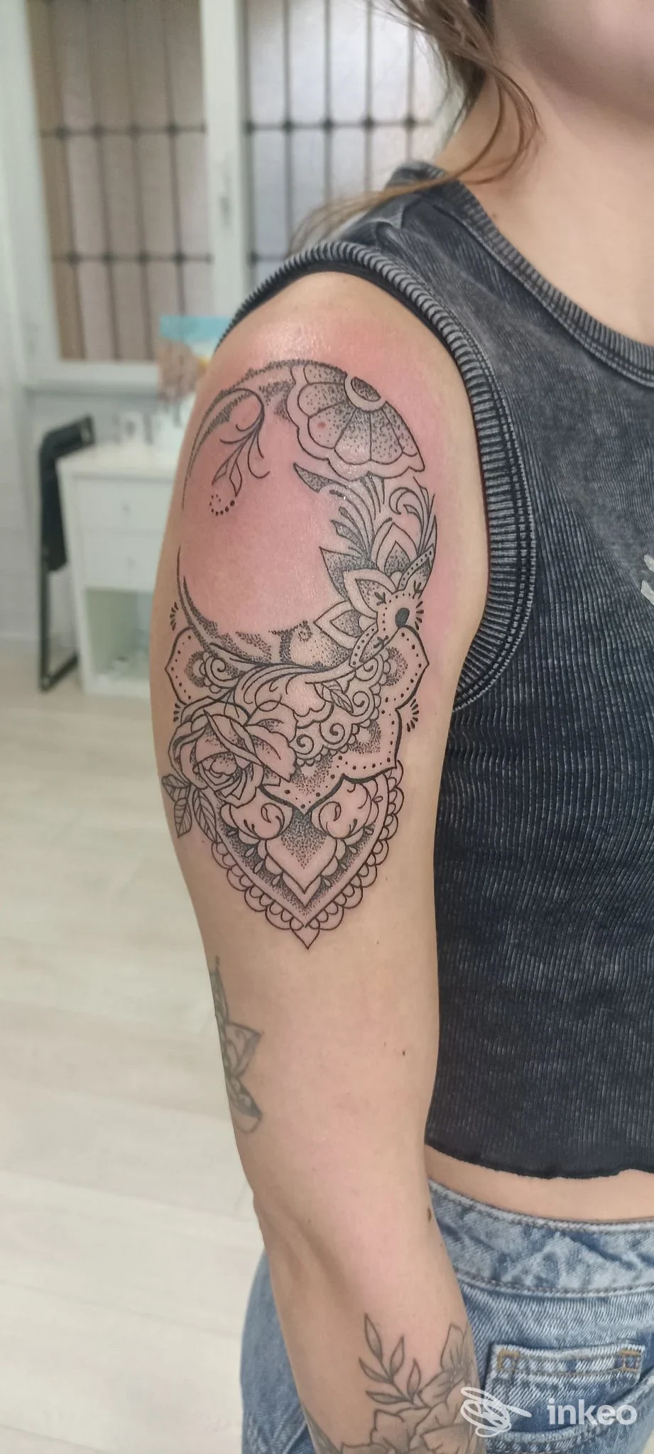 Tattoo ornamentale sull'avambraccio superiore di una persona, disegno in stile linework e motivi floreali, senza visione del volto, ambientazione interna neutra.