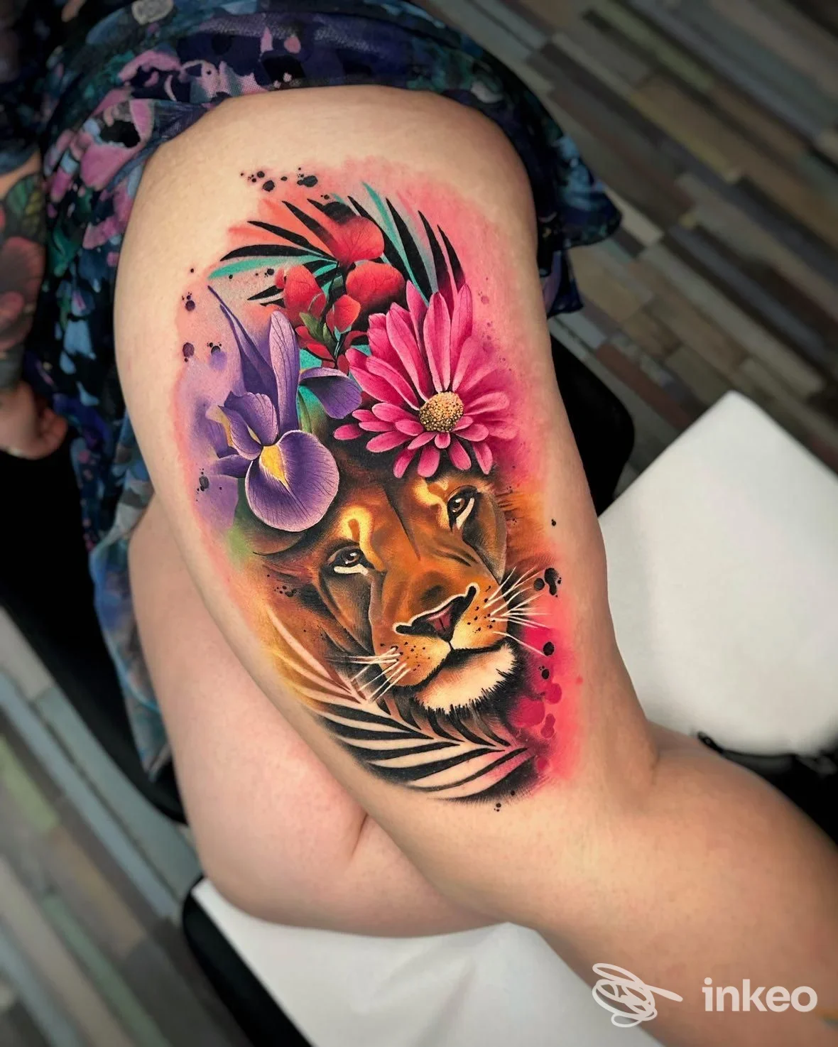 Tattoo a braccio raffigurante una tigre con fiori colorati, eseguito sulla pelle della persona, senza overlay o fotografie di schermi; vivaci sfumature rosse e viola sullo sfondo.