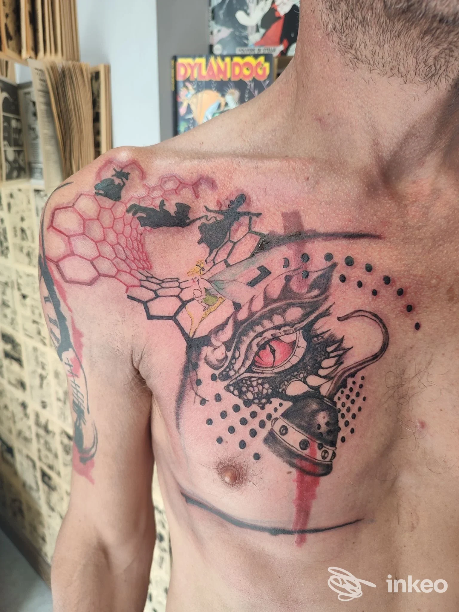 Tattoo visibile sulla pelle del torace e della spalla sinistra, stile misto tra geometrico e figurativo, con colori rosso e nero.