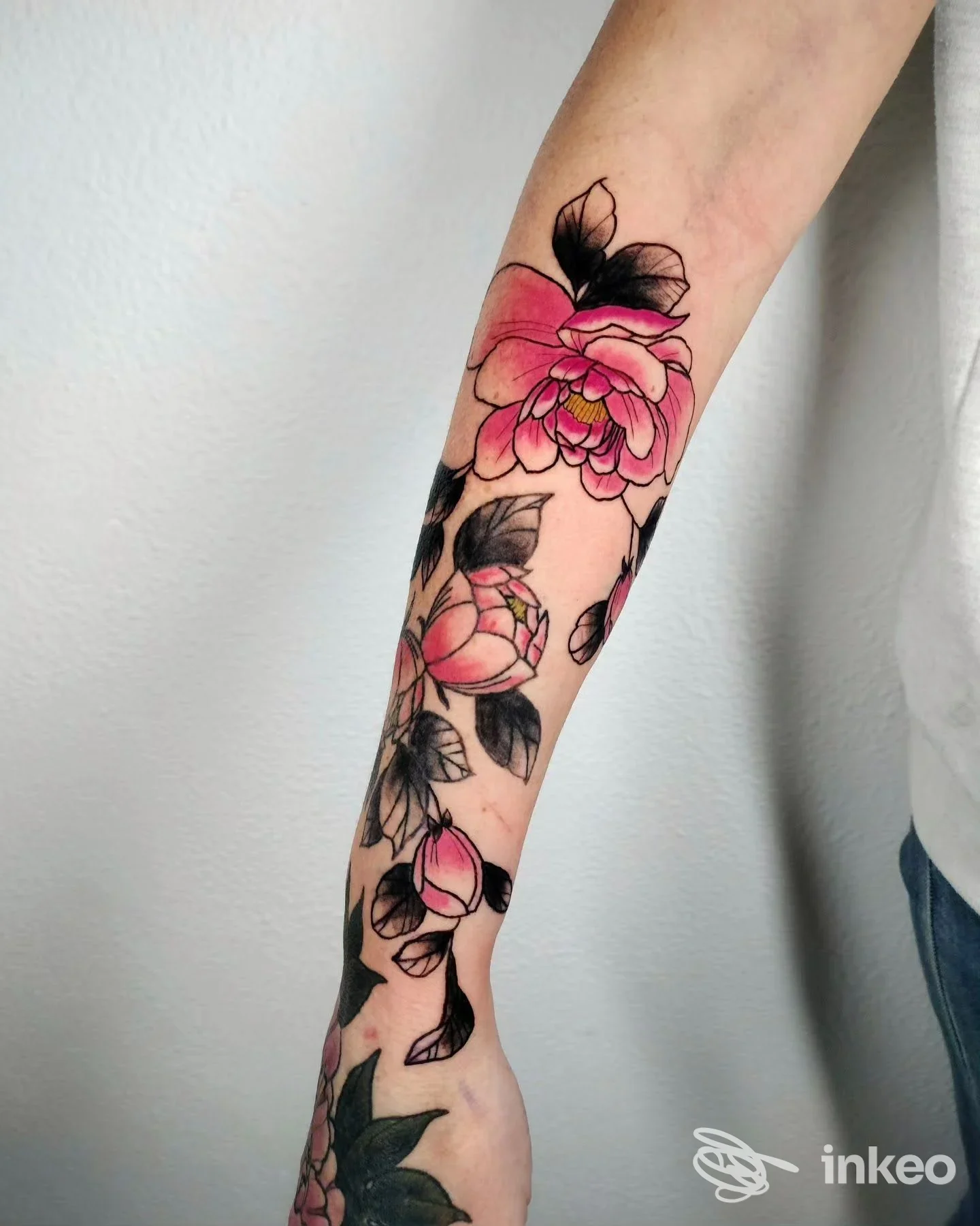 Tattoo floreale rosa su avambraccio, contorni neri definiti e foglie verdi, ritratto su pelle esposta senza volto visibile.
