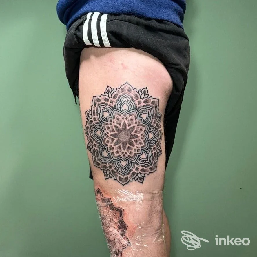 Grande tatuaggio mandala nero sulla coscia destra, in guarigione, parzialmente coperto da cerotto trasparente.
