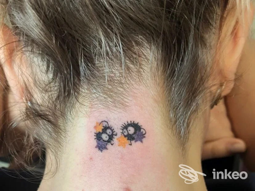 Due tatuaggi a forma di piccoli fiori blu con petali viola e stelle gialle sulla nuca, realizzati sulla pelle, senza presenza di viso visibile.