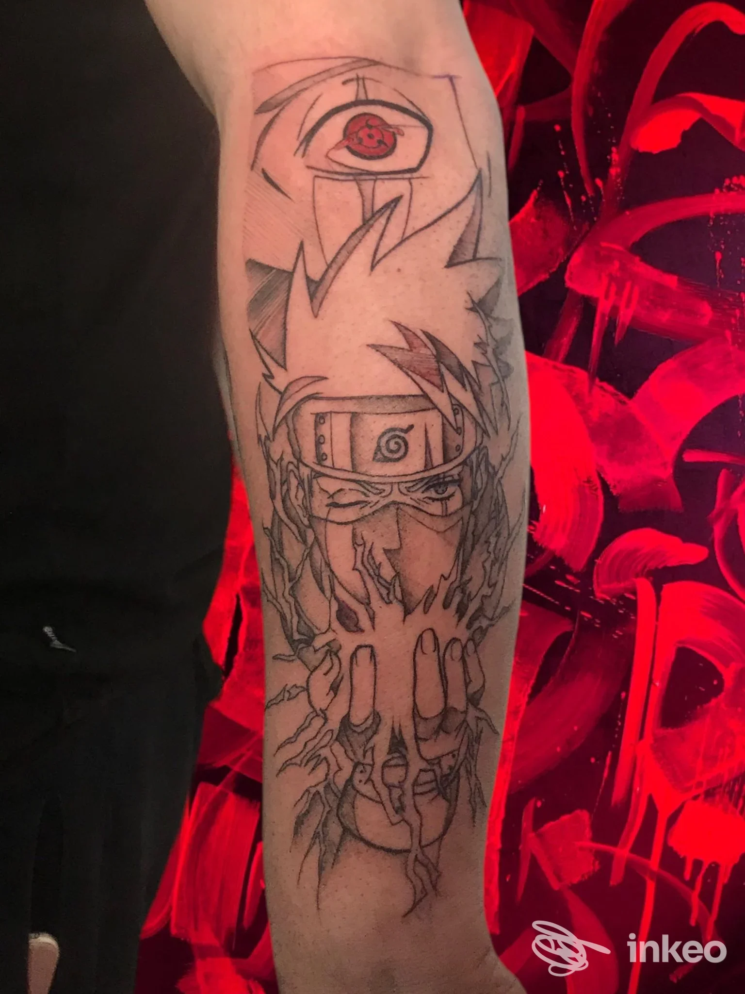 Tattoo visibile sull'avambraccio: linea grafica con volto stilizzato e occhio rosso in alto, disegno narrativo su pelle reale, nessuna interfaccia o testo sovrapposto, scatto chiaro.