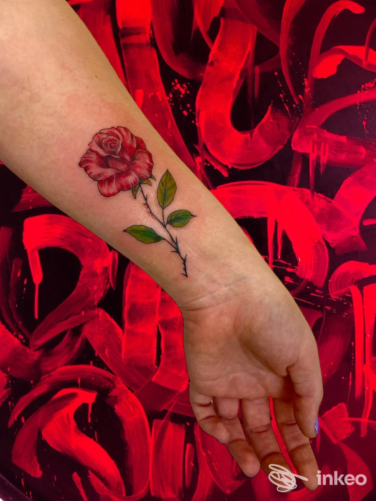 Tattoo su avambraccio raffigurante una rosa rossa con foglie verdi, su sfondo rosso e nero.