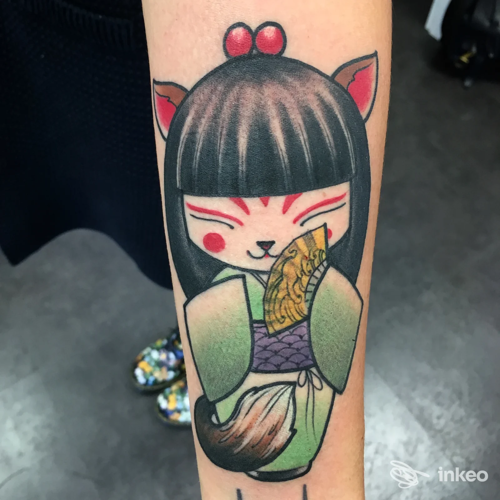 Tatuaggio su avambraccio di una creatura in stile kawaii che tiene una fetta dorata, con colori vividi e contorni neri definiti.