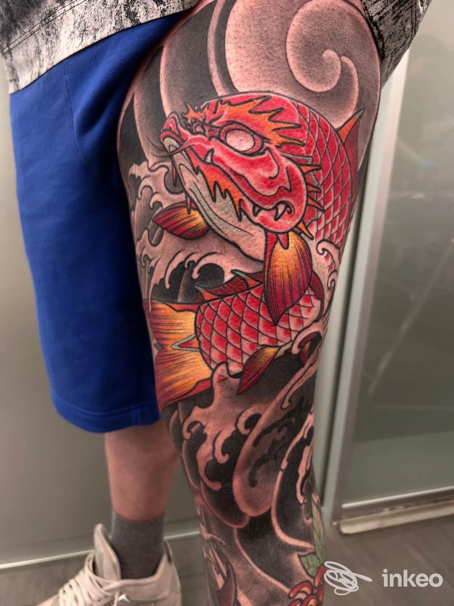 Tatuaggio di pesce drago colorato su gamba, tatoo ben definito su pelle, senza volto visibile. Pubblicato da Fastcolors Studio.