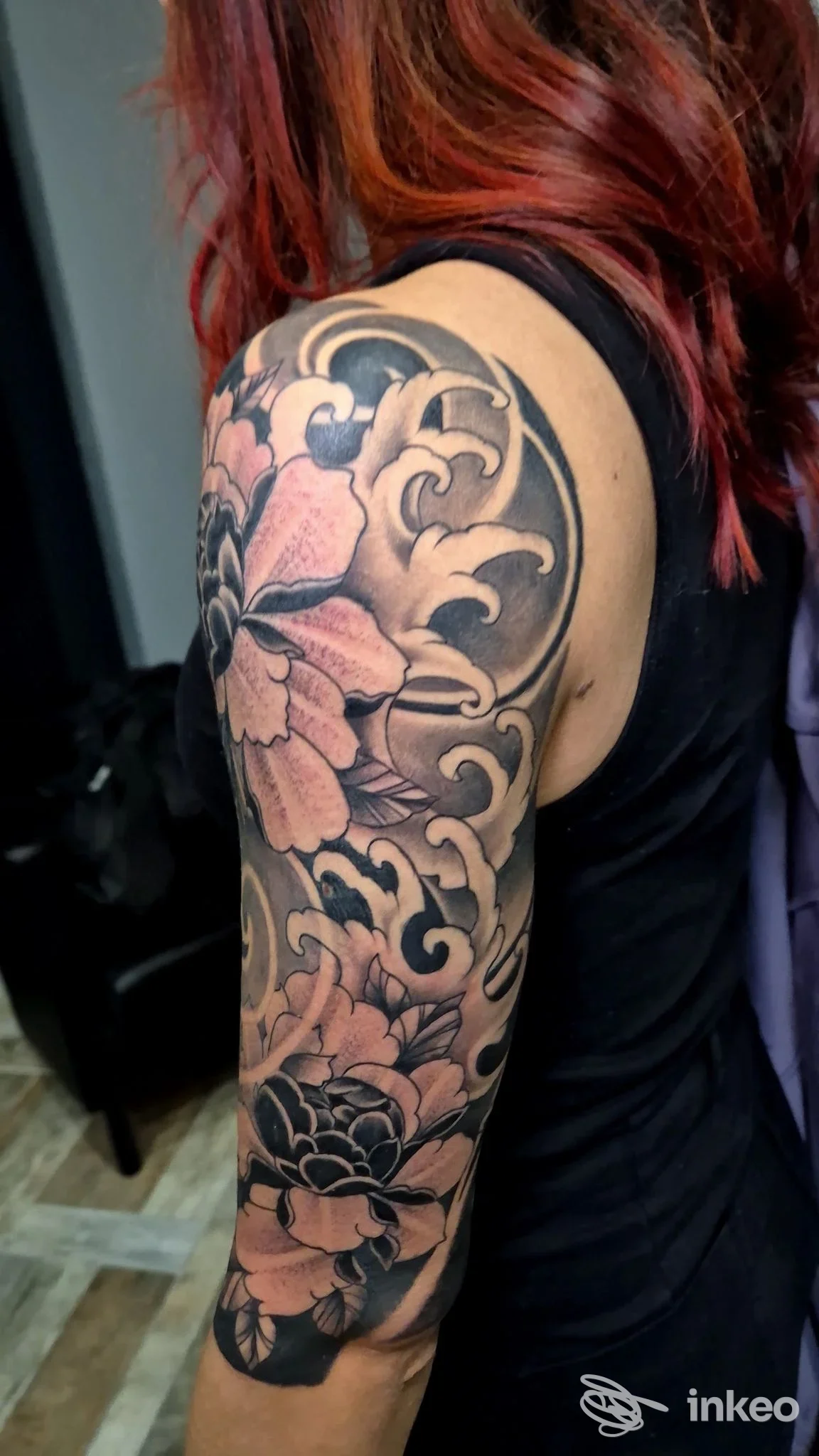 Tattoo floreale su braccio, fiori rosa con contorni scuri e motivi ondulati, tatuaggio visibile su pelle reale di una persona. Non si vede volto, solo braccio articulato.