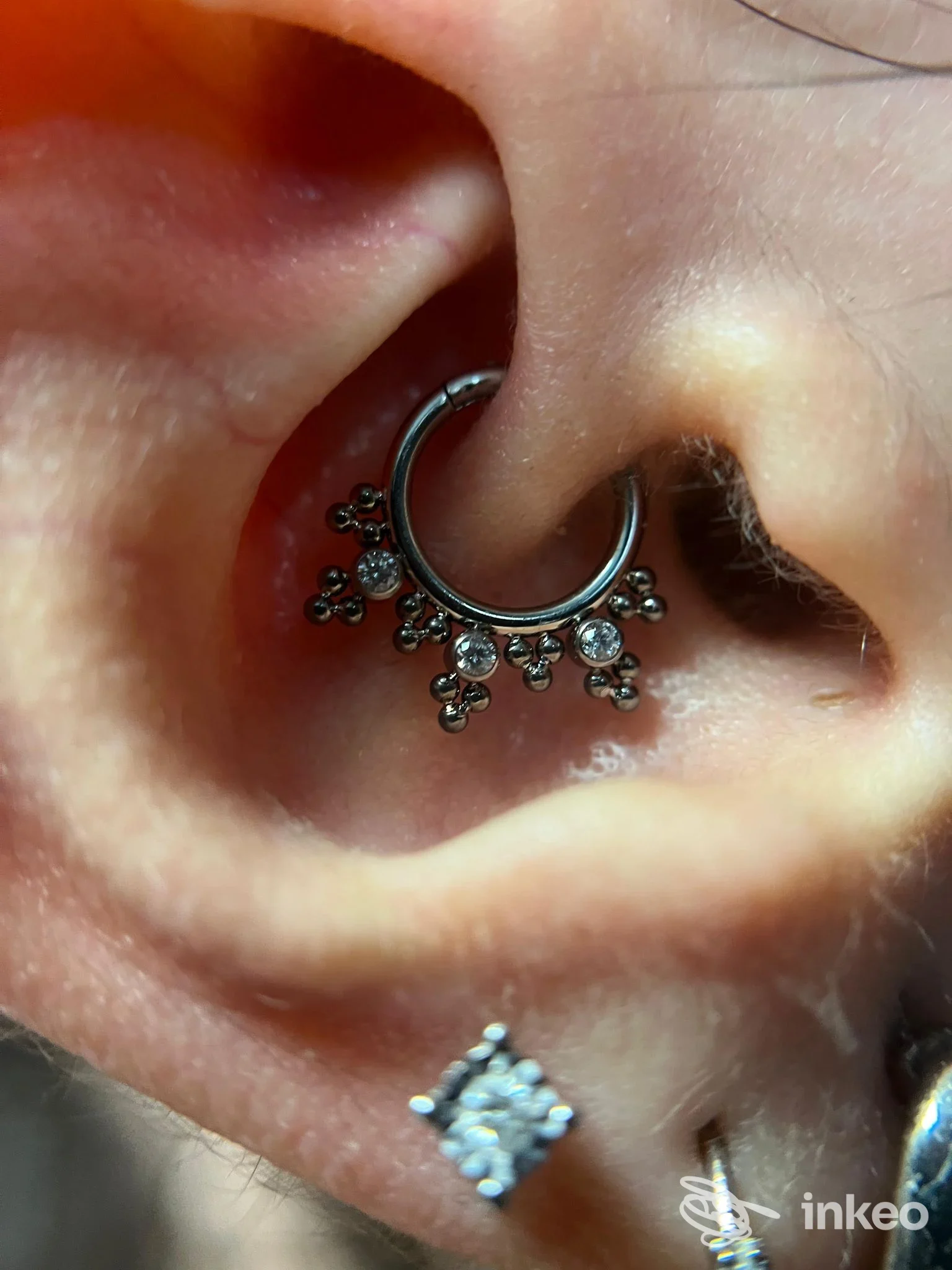 Primo piano su orecchio sinistro con piercing al cartilagine a anello e pendenti di zirconi, e un secondo piercings a livello del lobo.