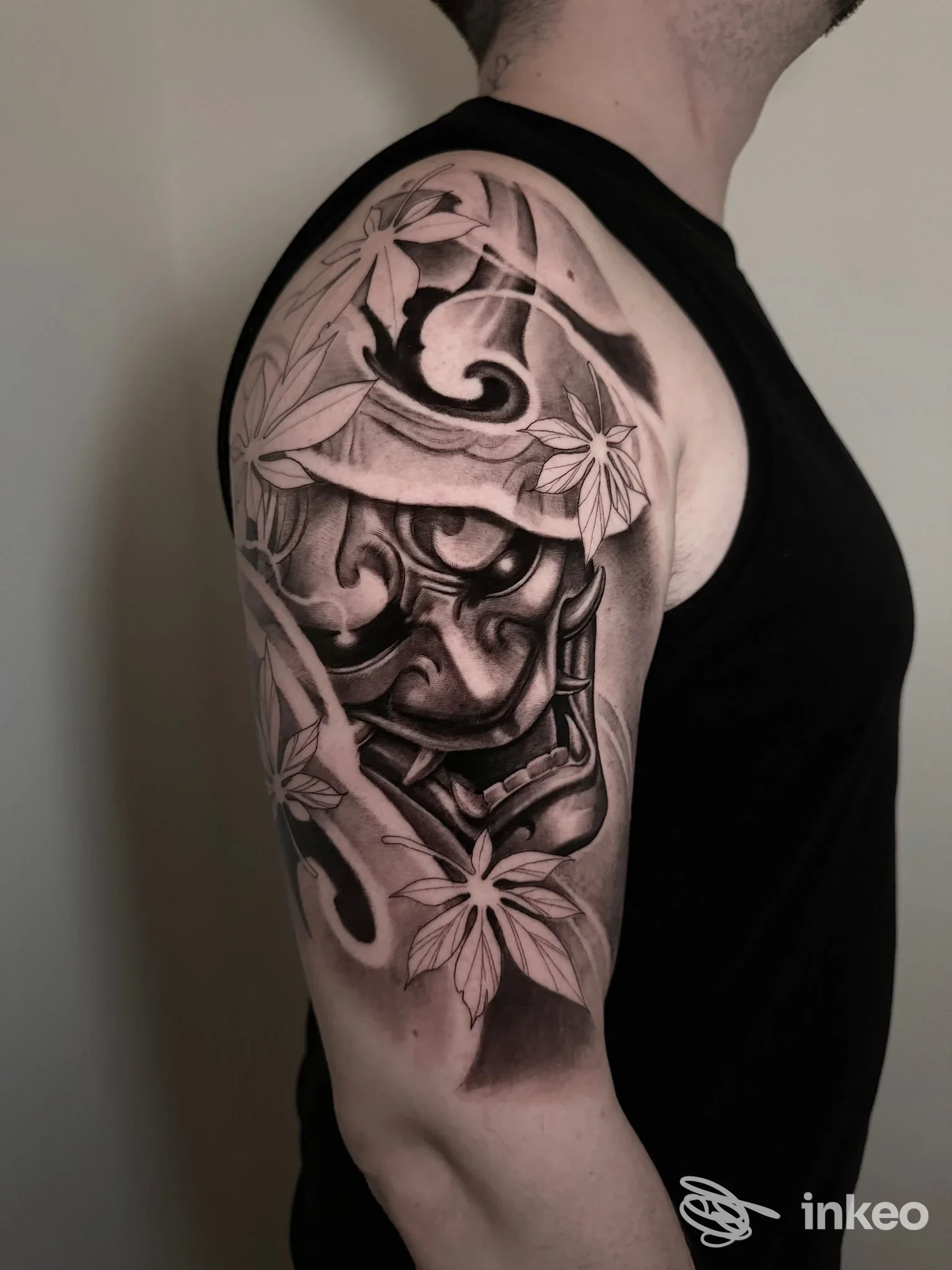 Tattoo sul braccio sinistro raffigurante ornamento floreale e motivi decorativi, visibile dalla spalla all'avambraccio, in toni neri e grigi.