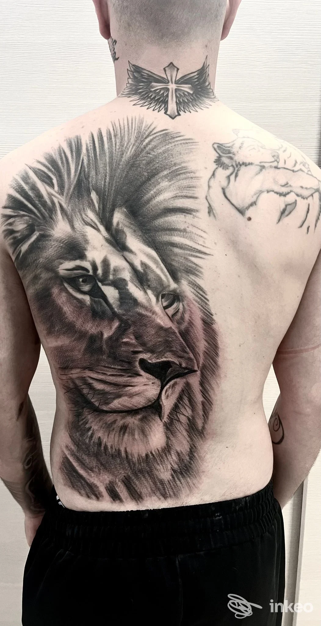 Tattoo realistico di leone sulla schiena con una croce sul collo, visibile solo la schiena del soggetto.