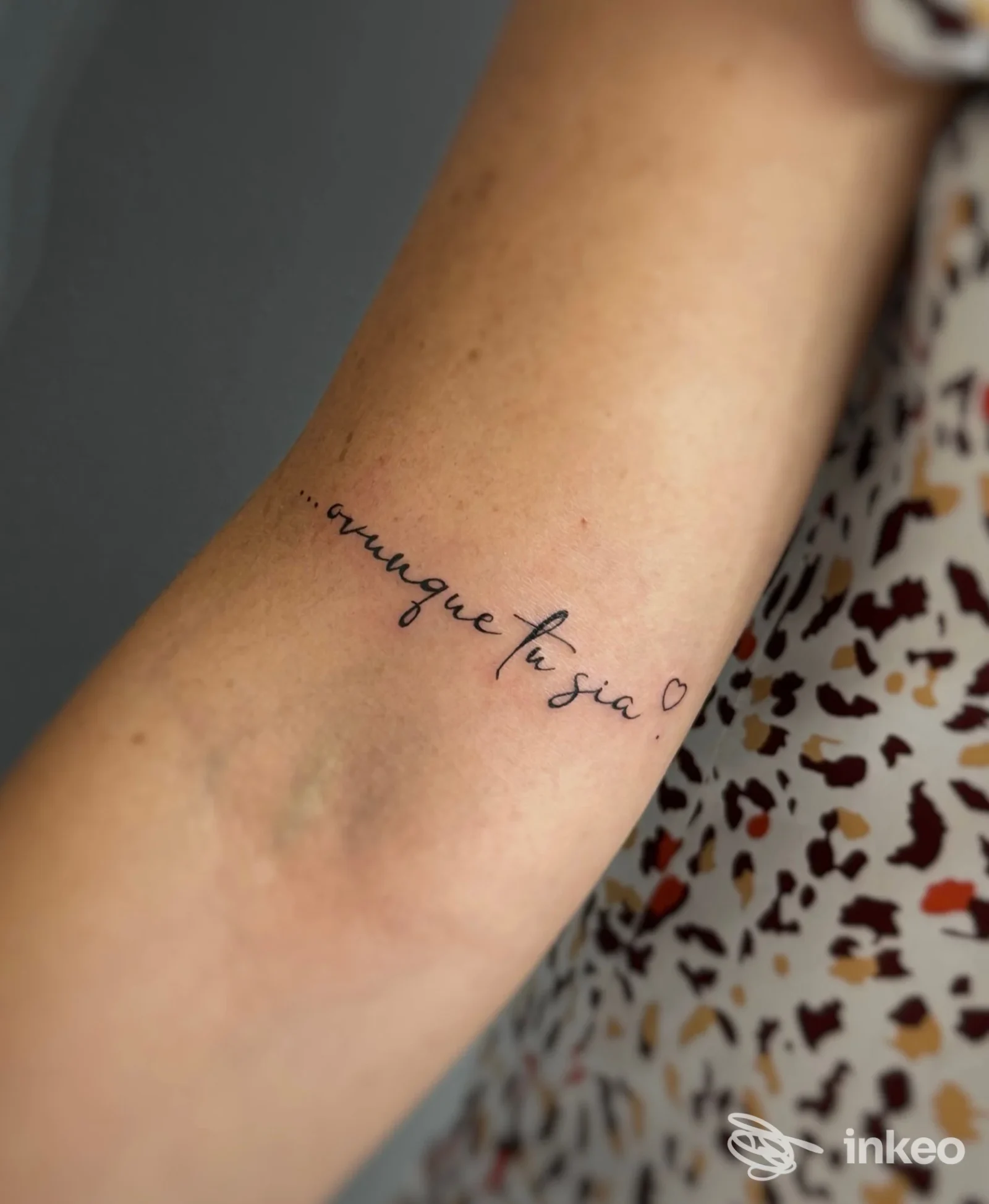 Tattoo minimalista in corsivo sull’avambraccio di una persona, realizzato direttamente sulla pelle, real billboard mostrata in primo piano.