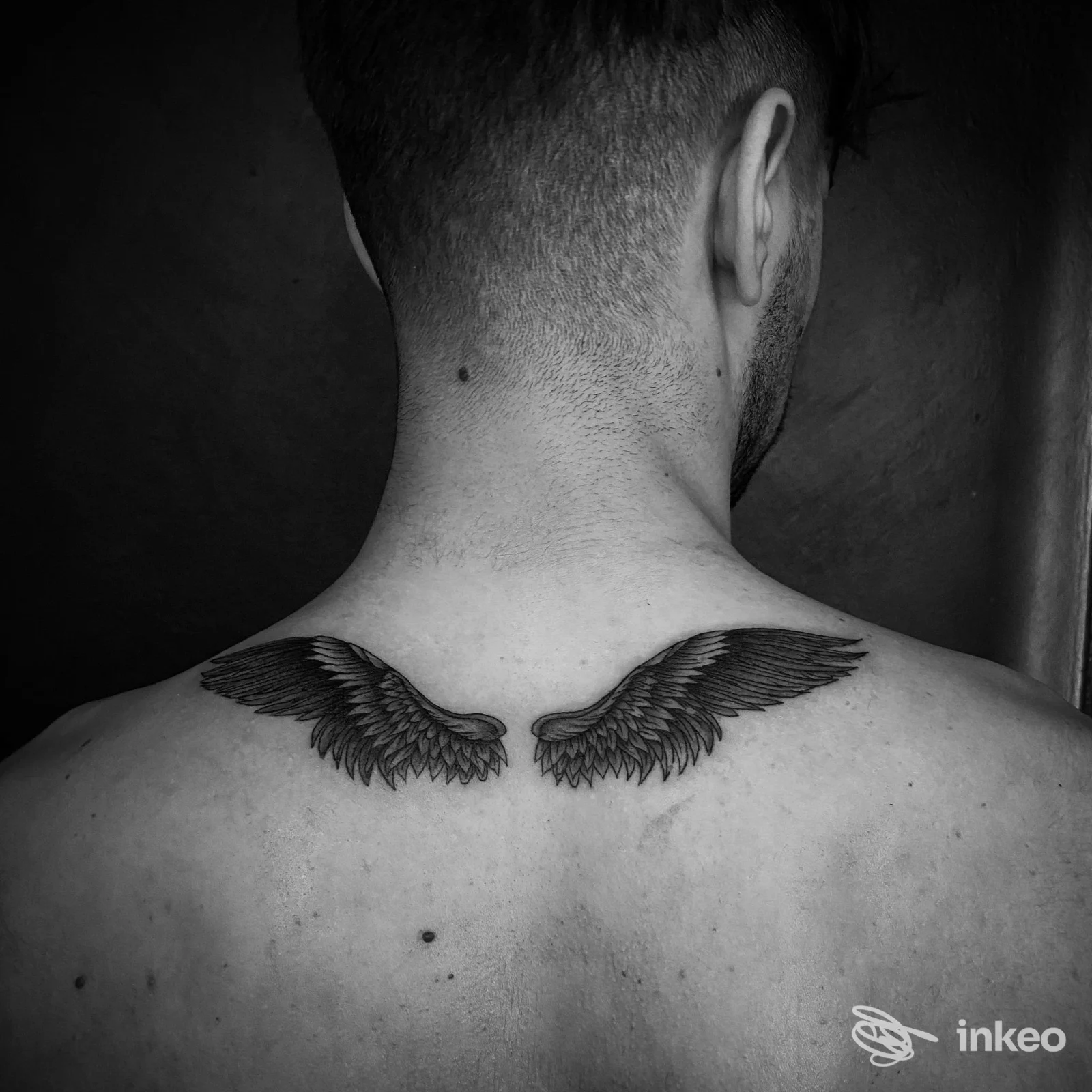 Tattoo sulle scapole raffigurante ali nere, visibile sul dorso di una persona visto di schiena, in bianco e nero.