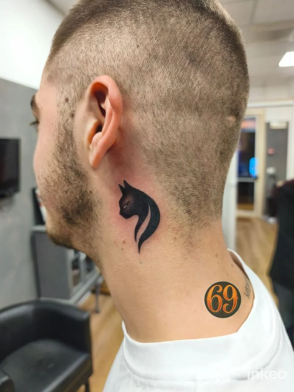 Tattoo nero a forma di cavallo sulla nuca/collo posteriore di un uomo, visibile lateralmente; si distingue anche un altro tatuaggio circolare con numero 69 sul bordo della spalla.